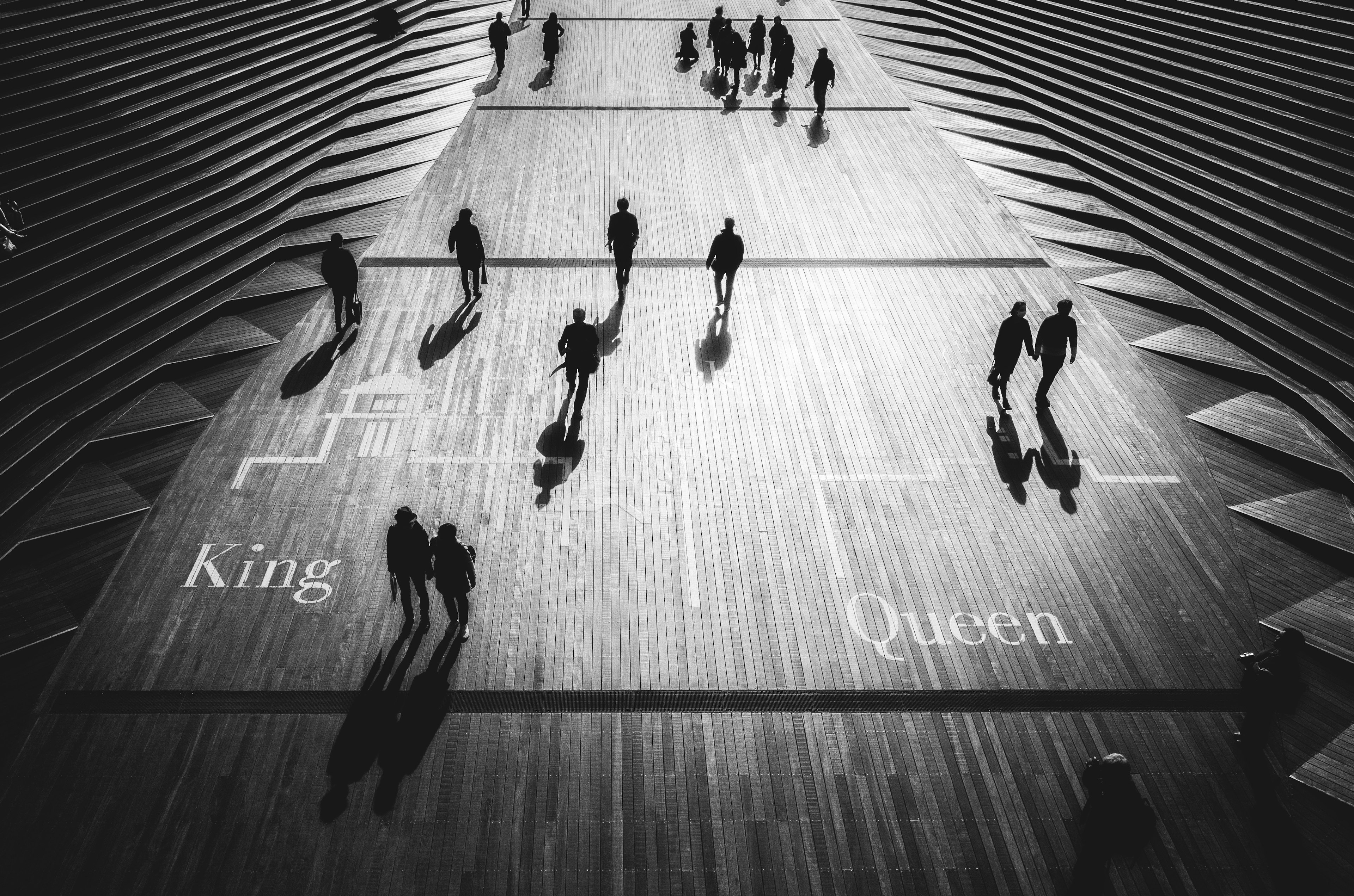 Imagen en blanco y negro de personas caminando por una calle con sombras y las palabras Rey y Reina