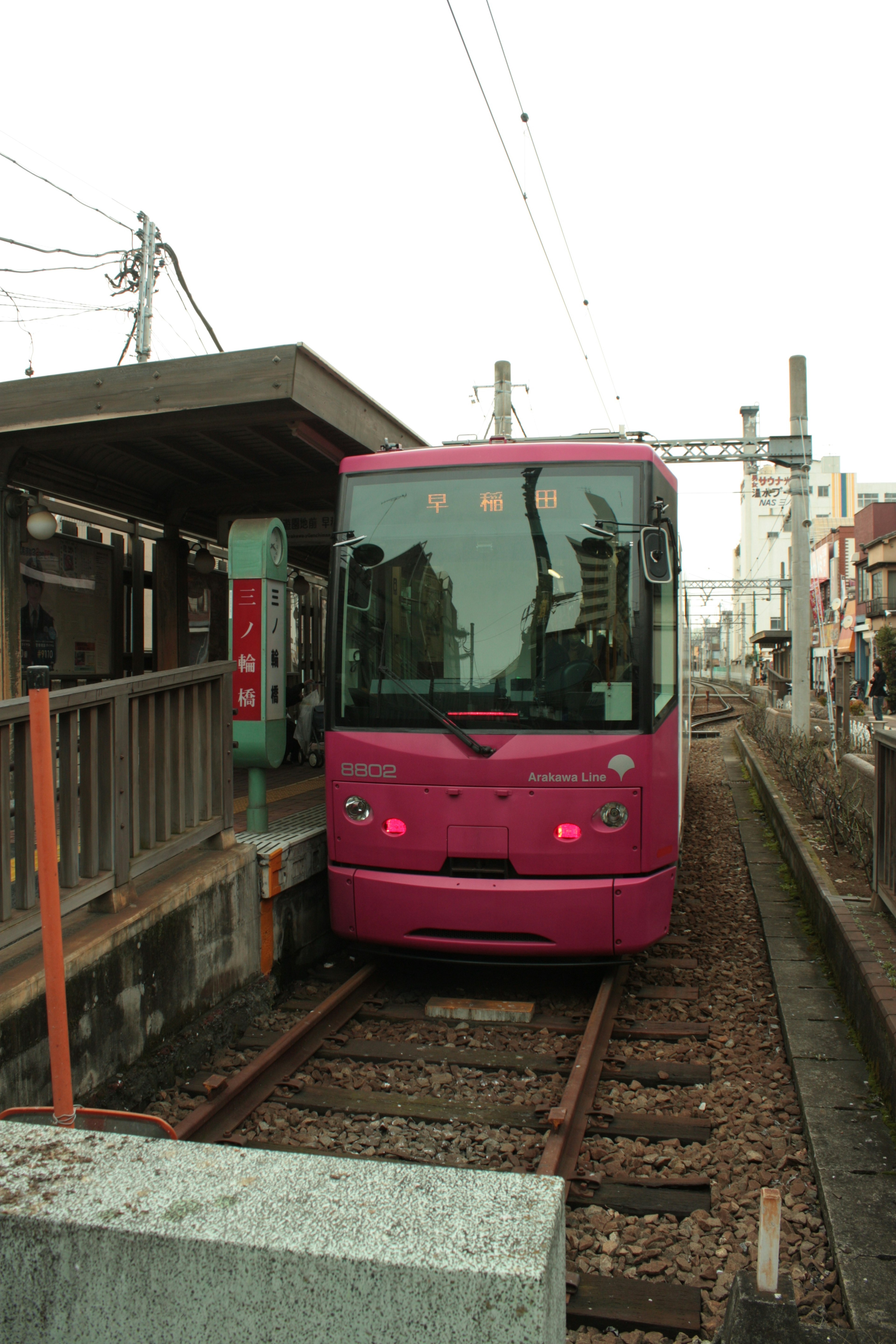 Sebuah kereta berwarna pink berhenti di stasiun dikelilingi bangunan perumahan