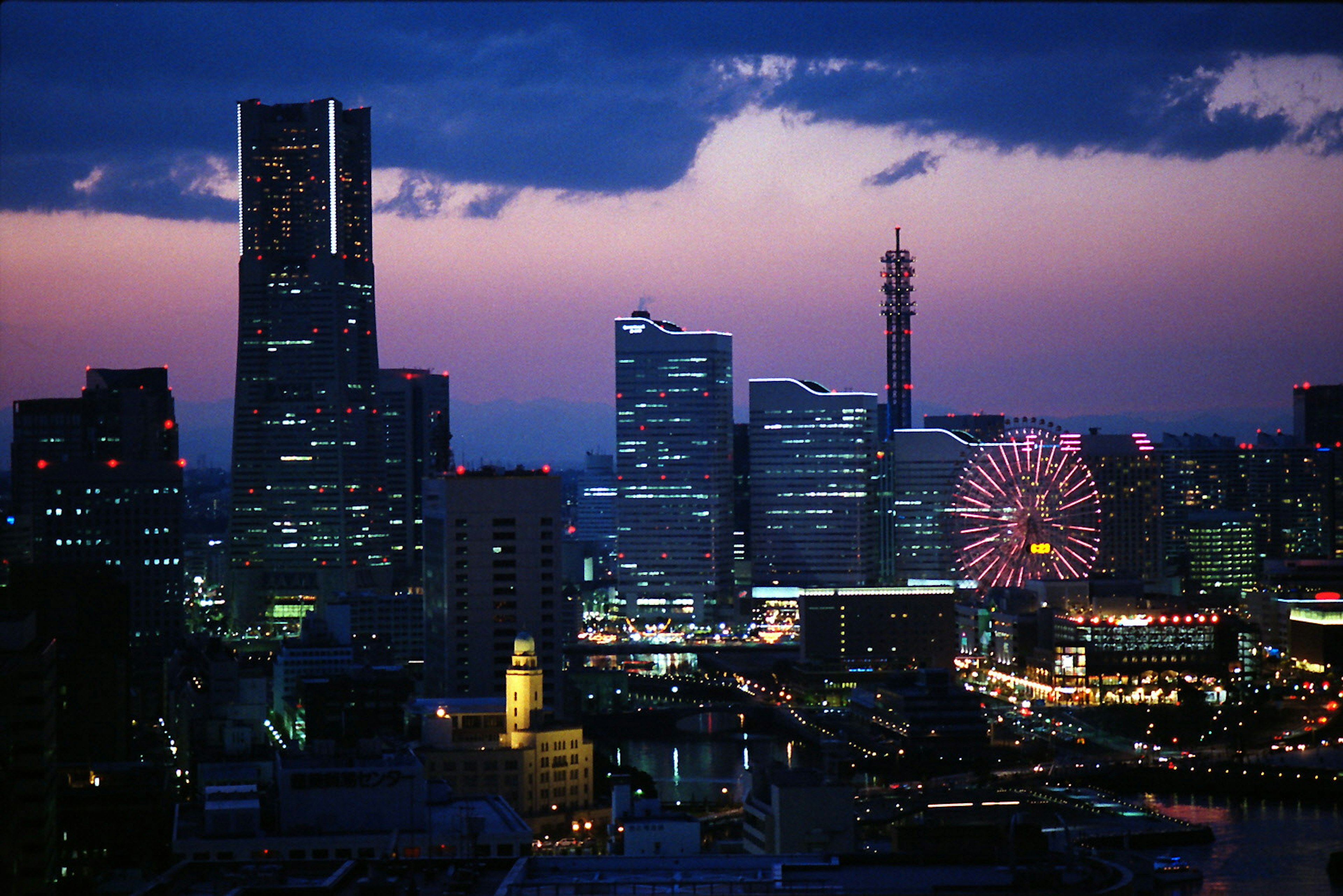 Skyline di Yokohama di notte con grattacieli e ruota panoramica sotto un cielo viola