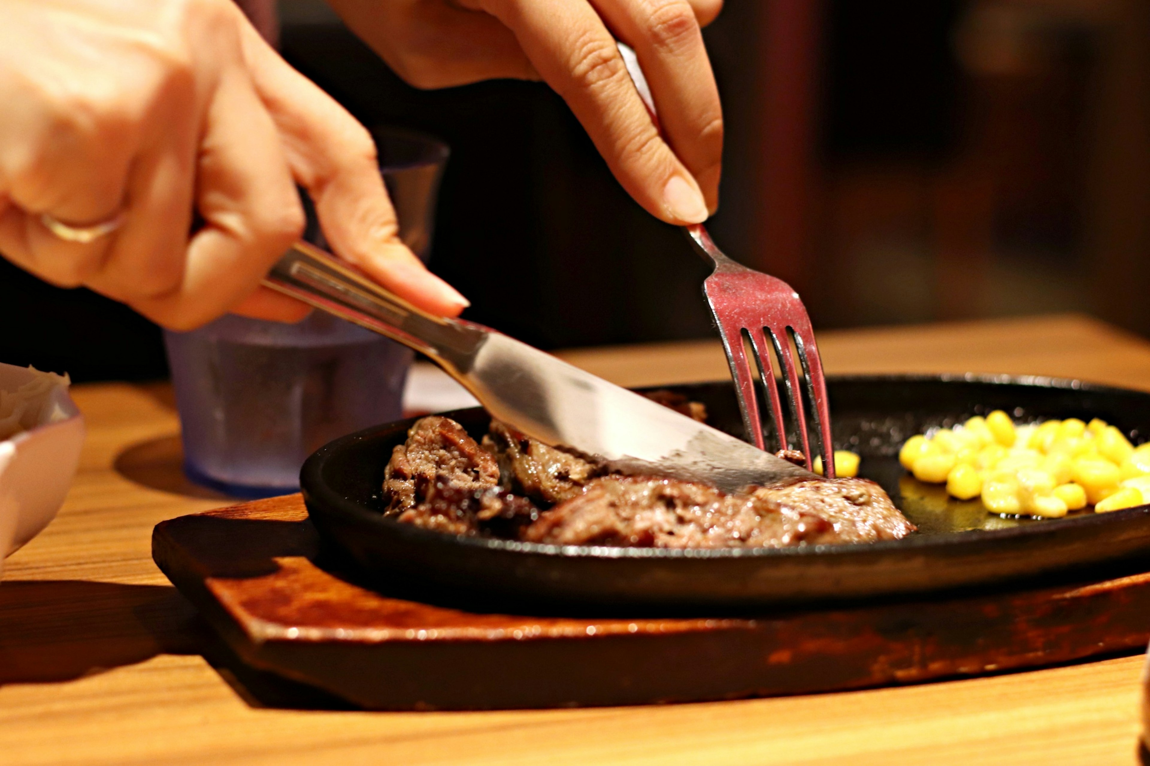 Hands cutting steak on a sizzling plate with corn