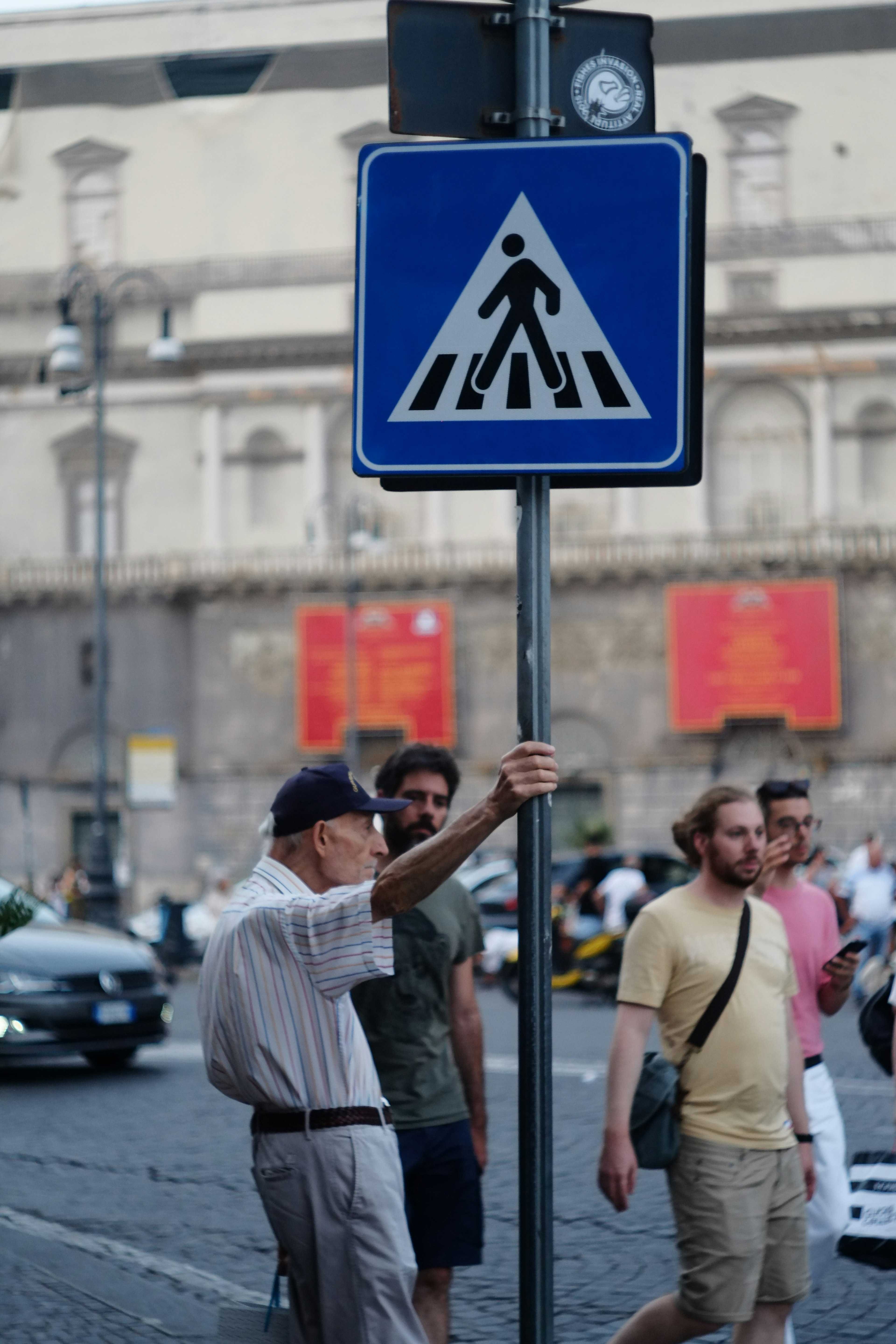 Elderly man standing by a pedestrian crossing sign with people walking by