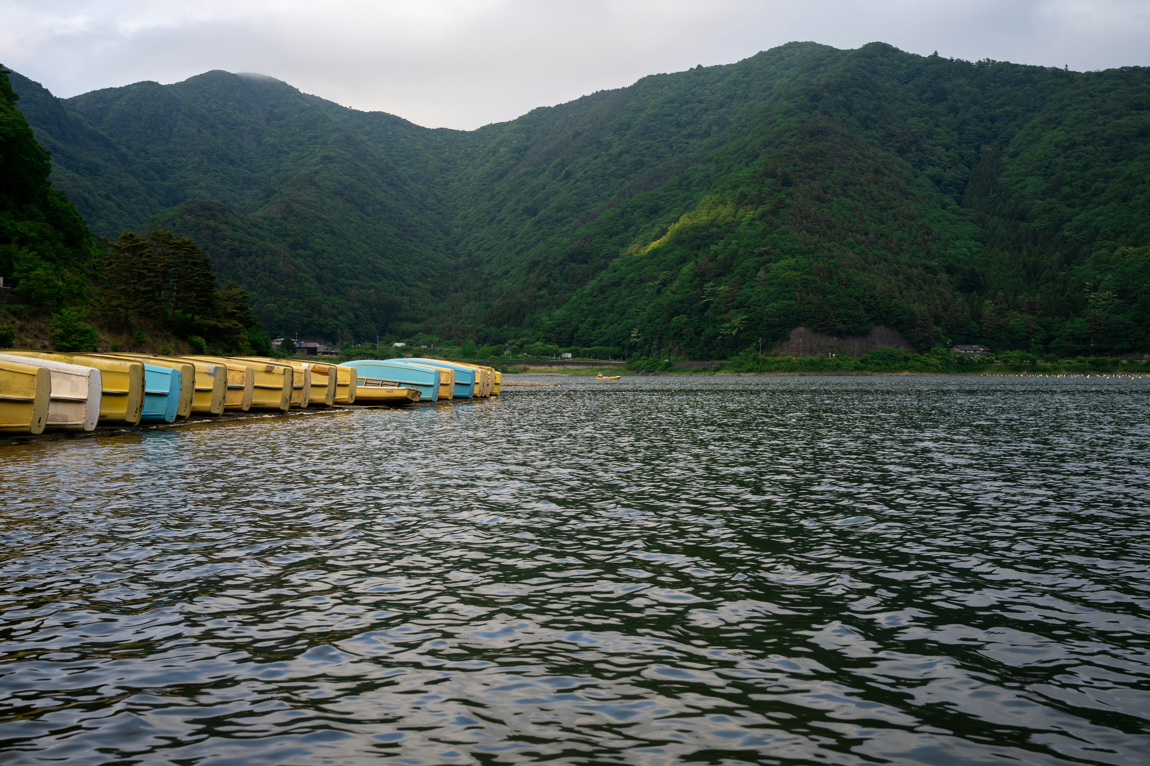 Perahu berwarna-warni di danau tenang dikelilingi gunung hijau