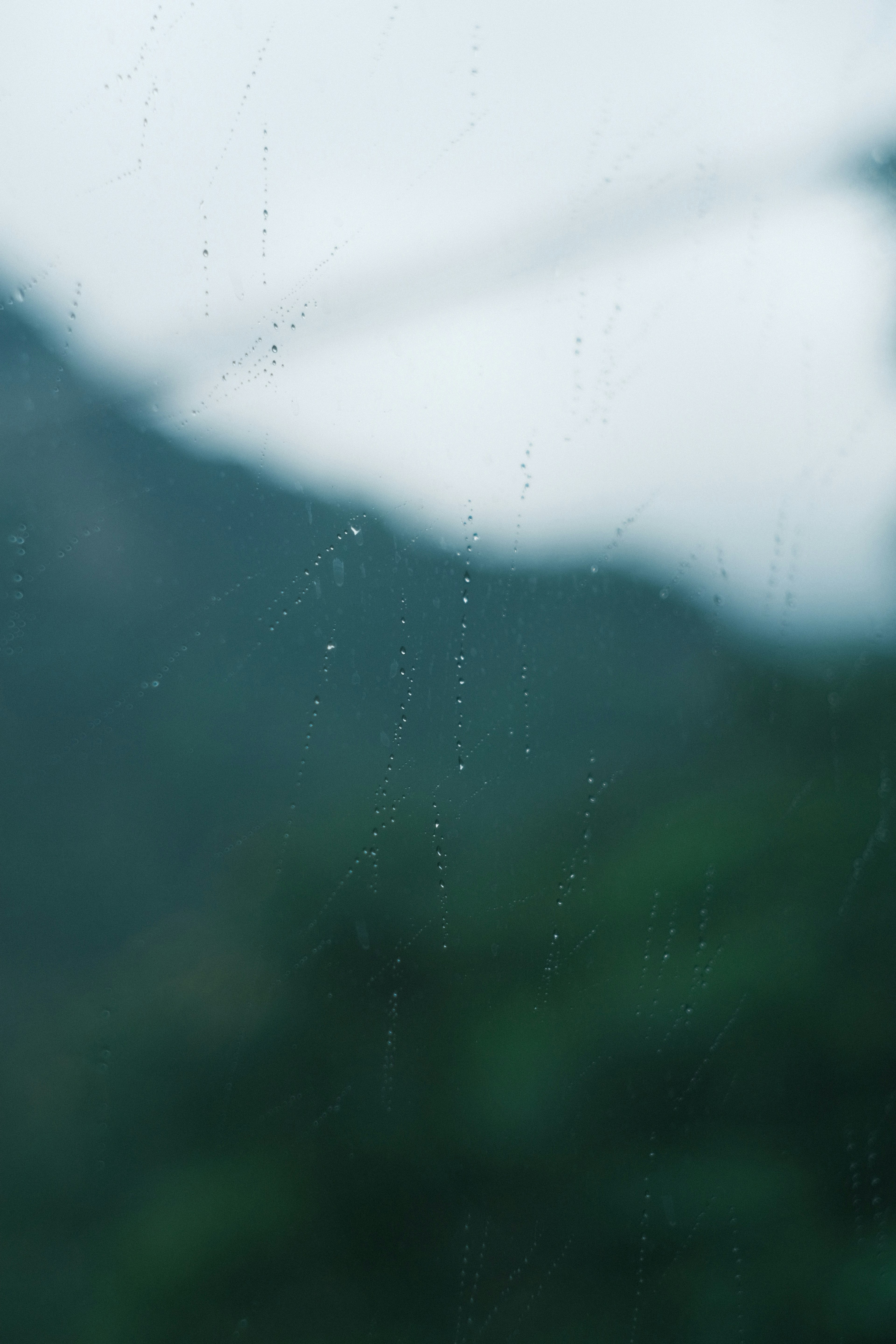 Gotas de lluvia en una ventana con montañas verdes borrosas al fondo