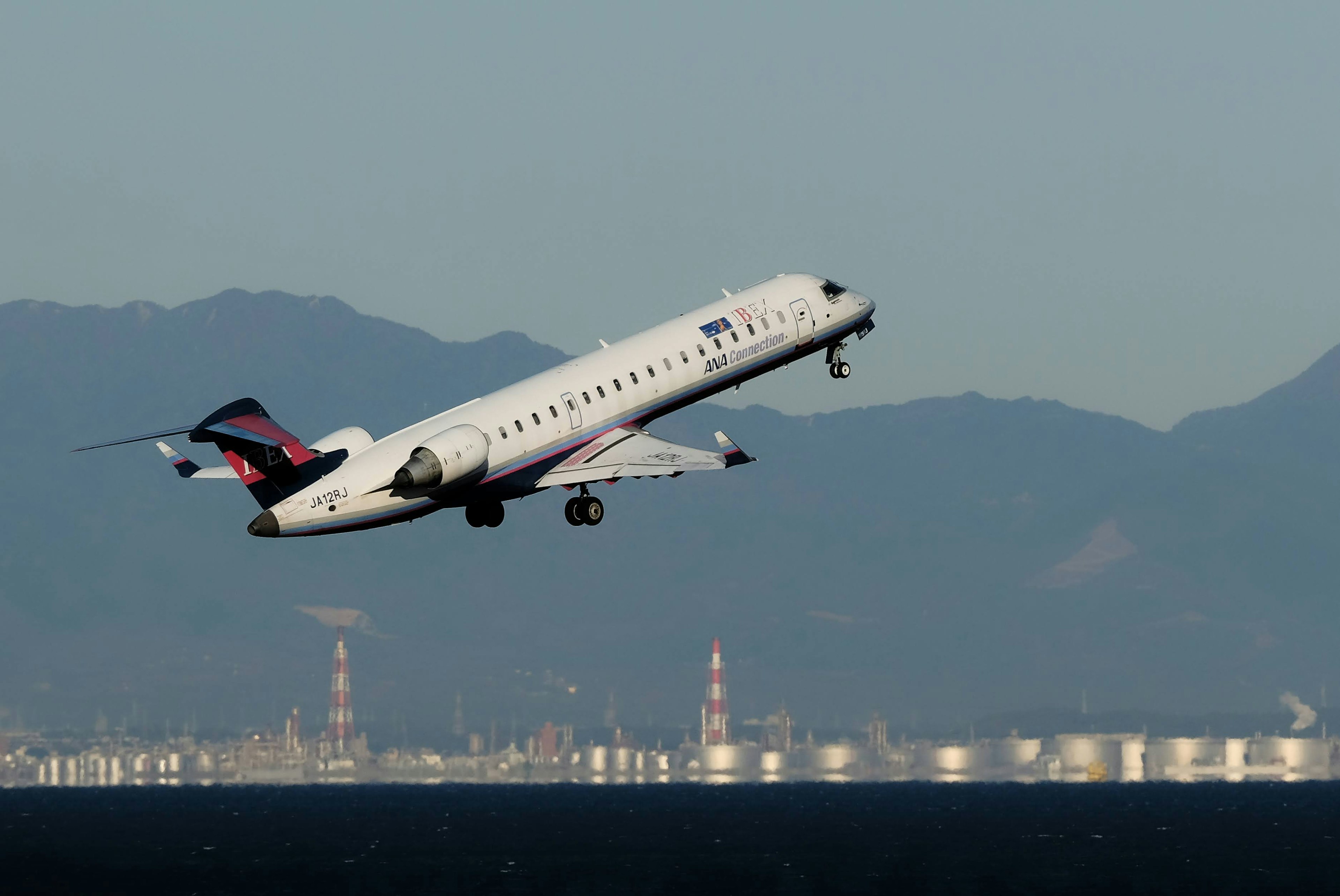 Flugzeug startet mit Bergen und Fabriken im Hintergrund