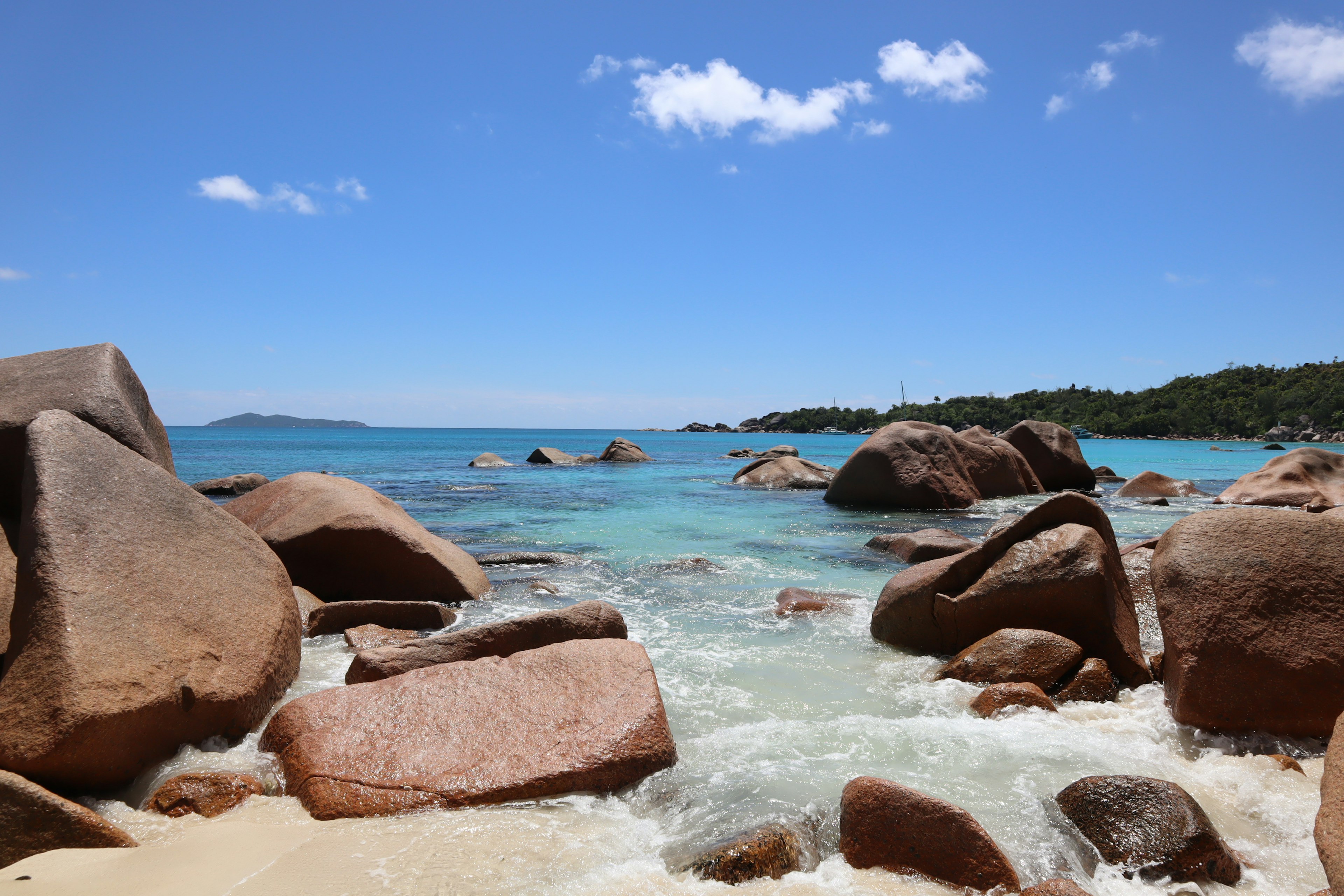 Large rocks between blue sea and white sandy beach