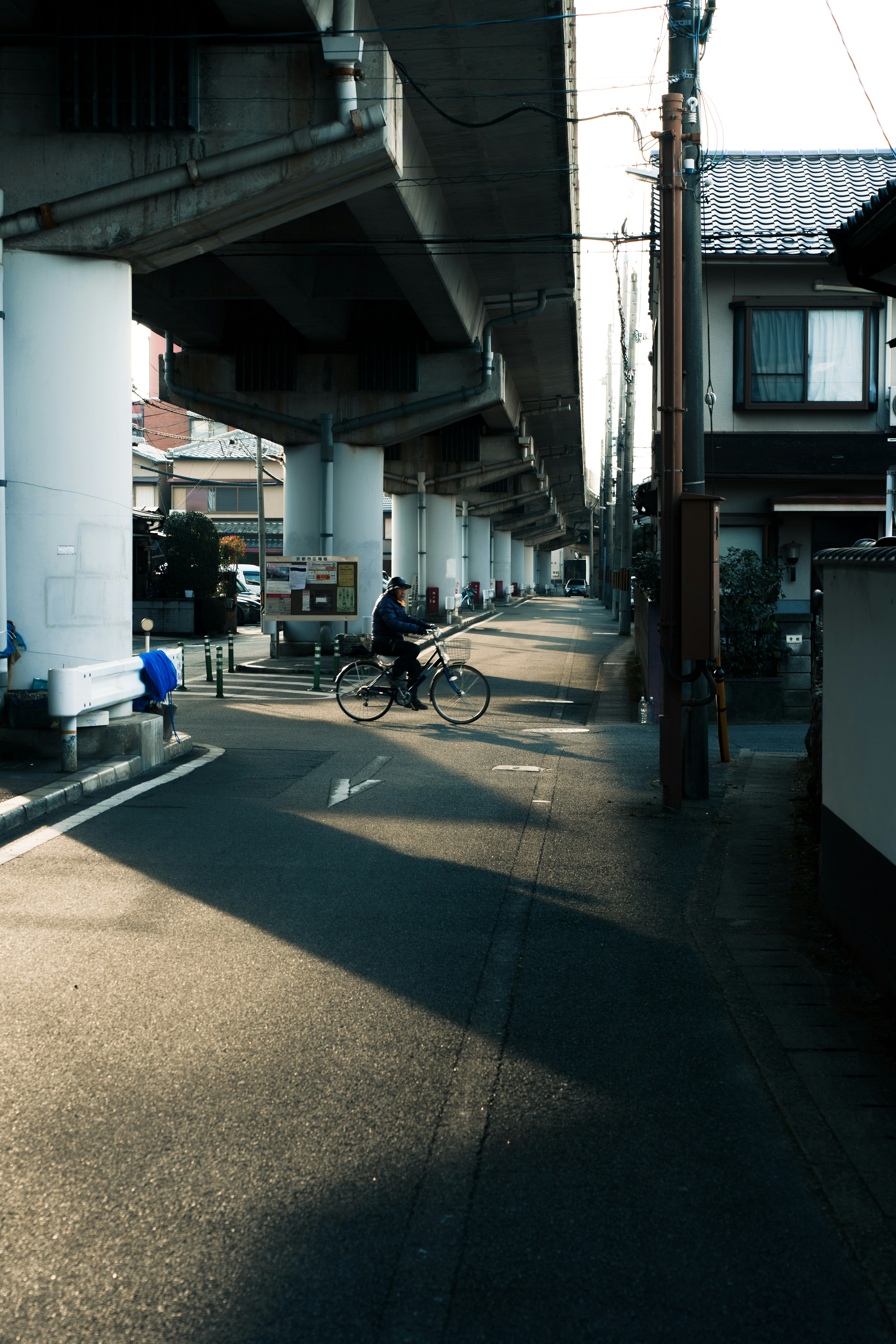 Scene of a person riding a bicycle on a road under an elevated structure