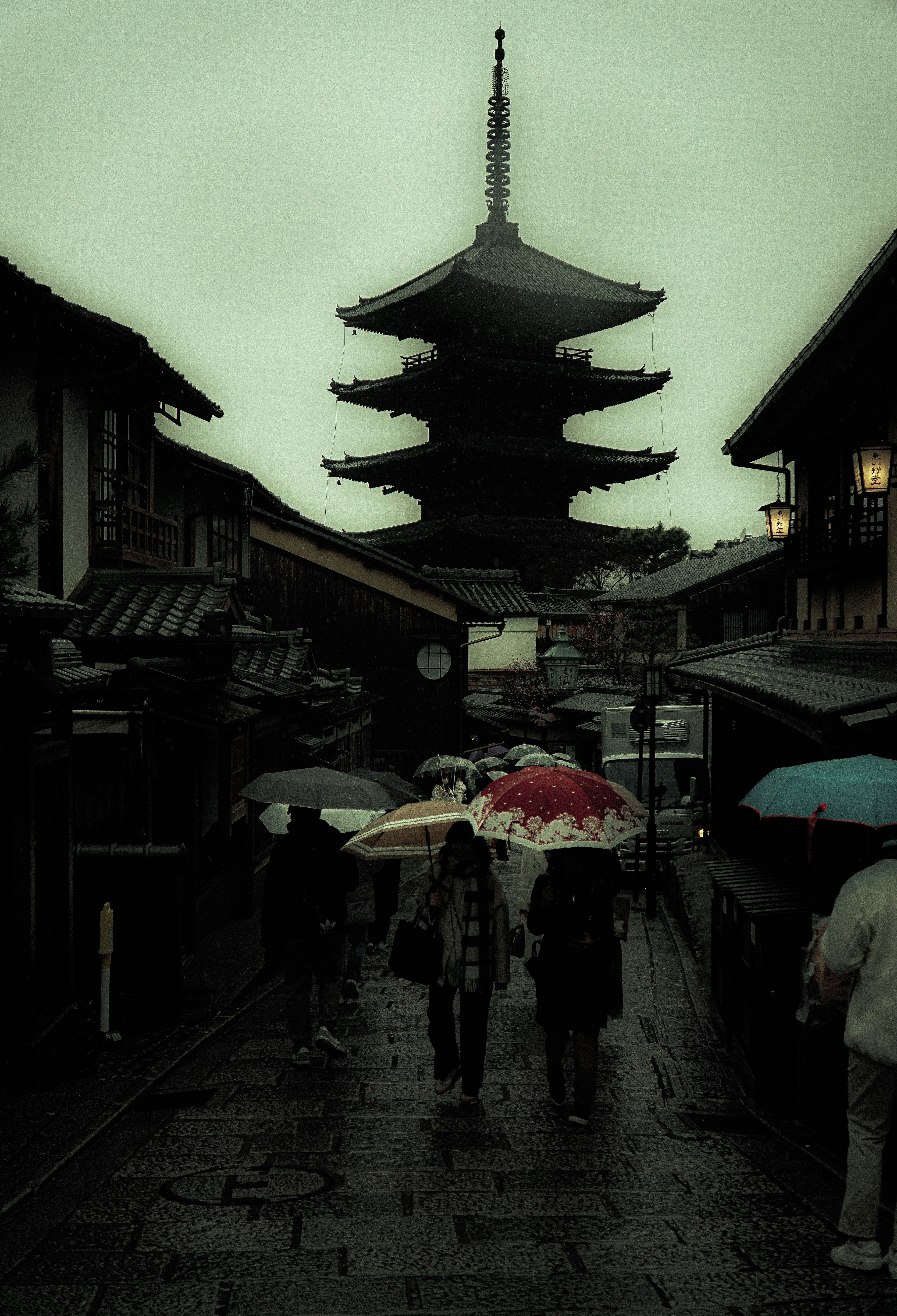 Silhouette of people with umbrellas near a pagoda in the rain