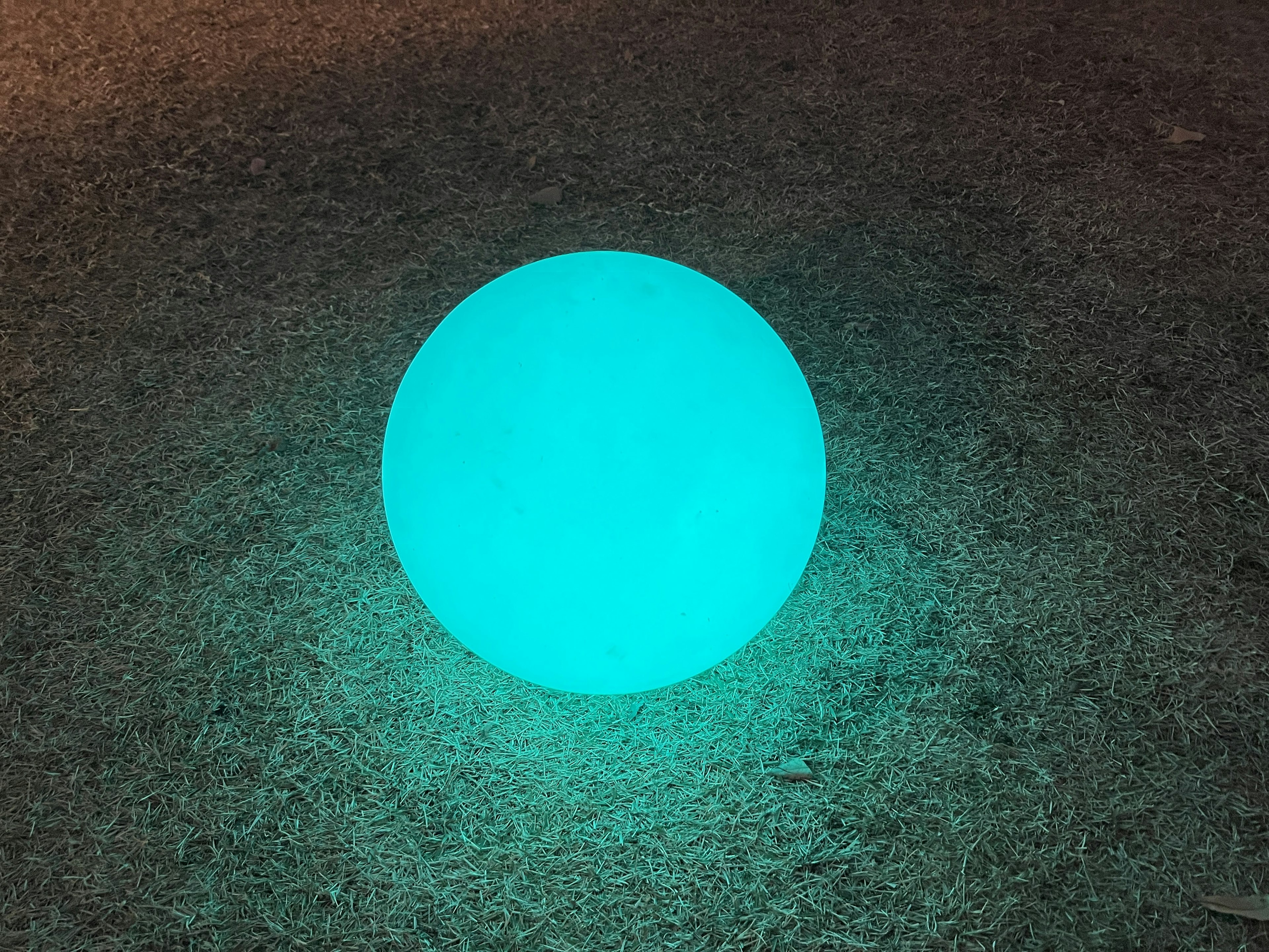 Une sphère teal lumineuse placée sur de l'herbe