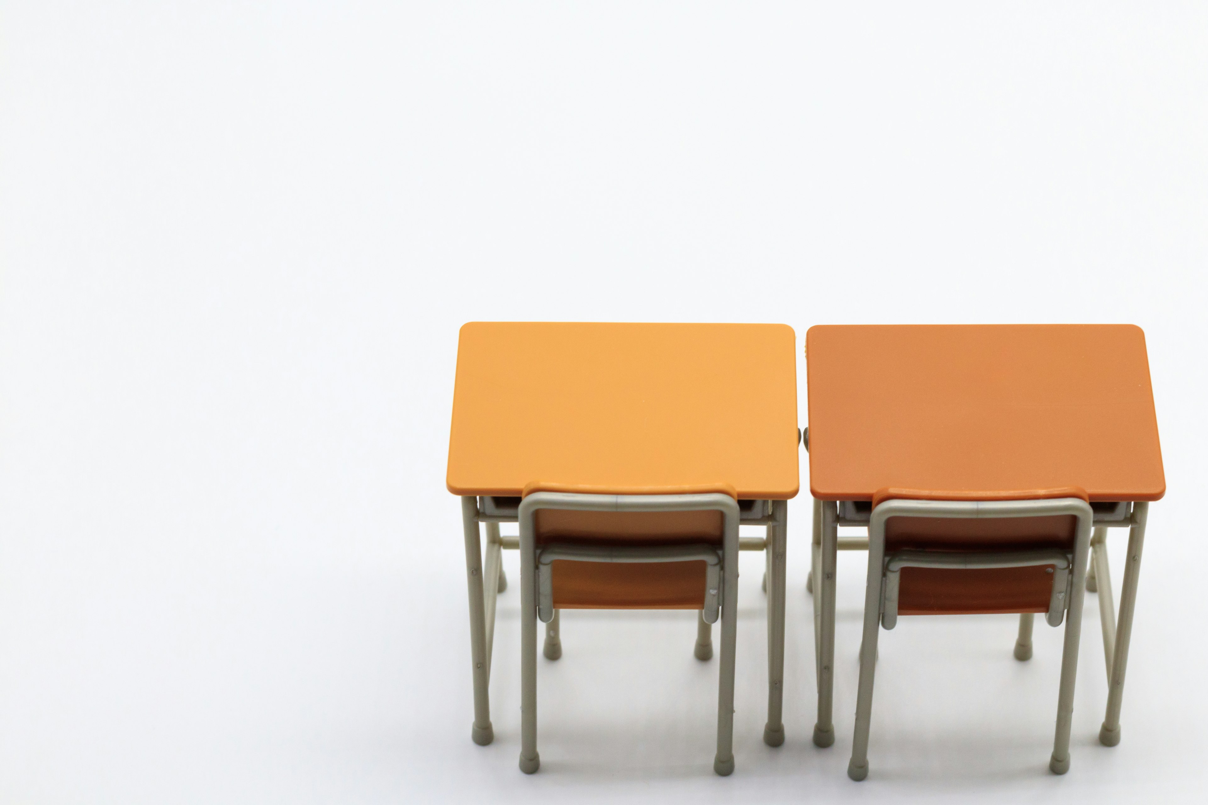 Two orange desks with chairs arranged in a minimalist classroom setting