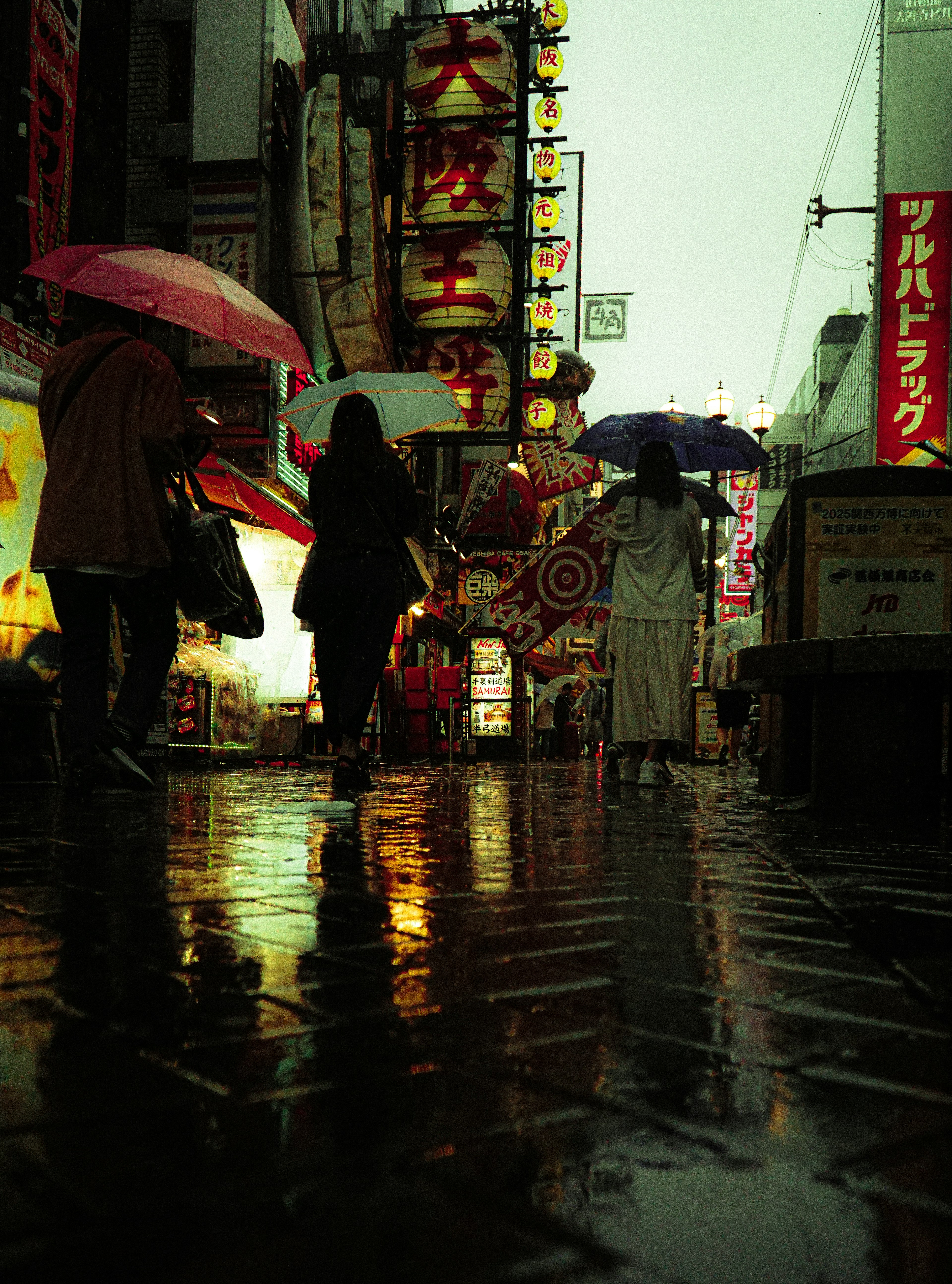 雨の中、傘を持つ人々が歩いている繁華街の風景