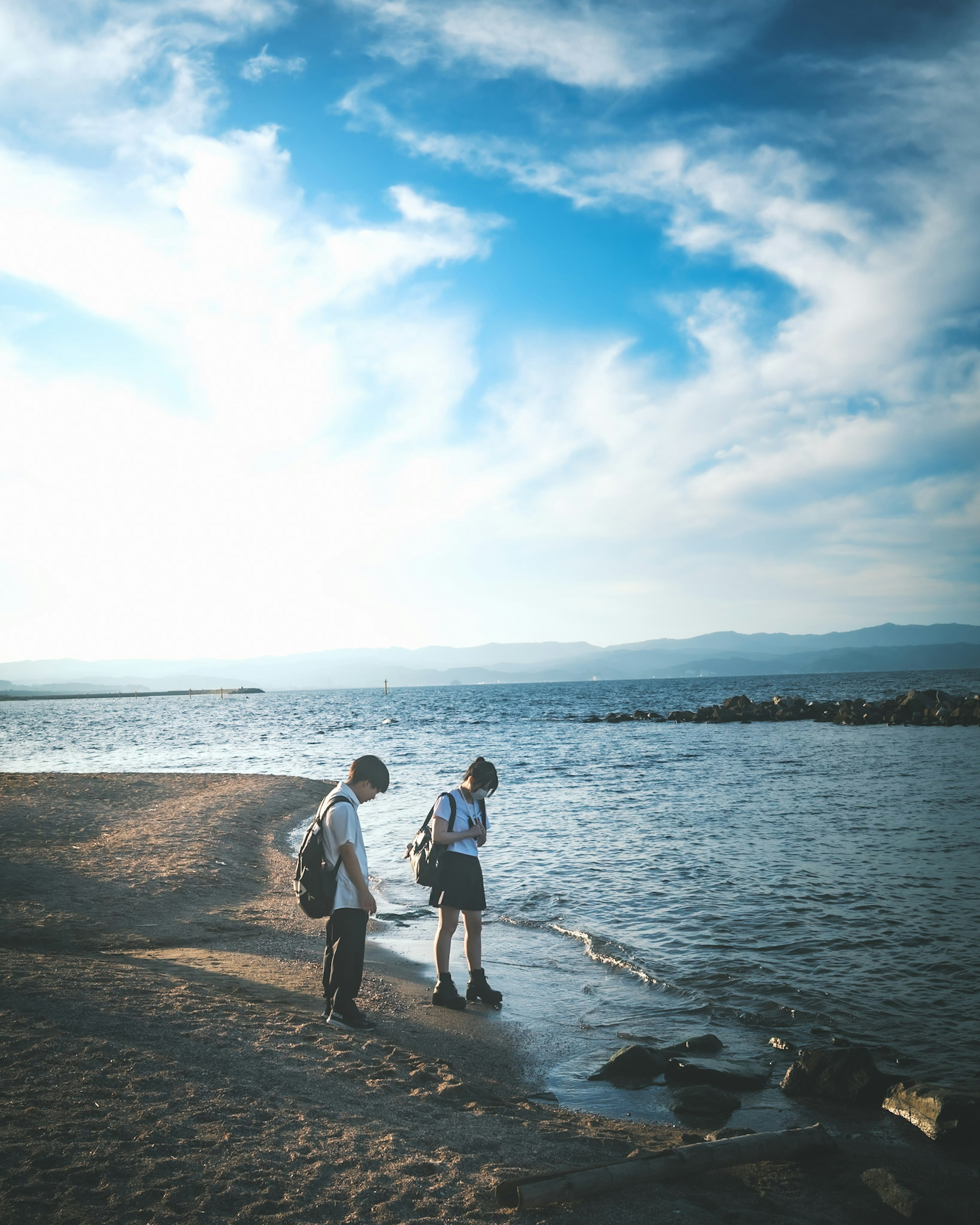 海岸で水辺を歩く二人の人々と青い空