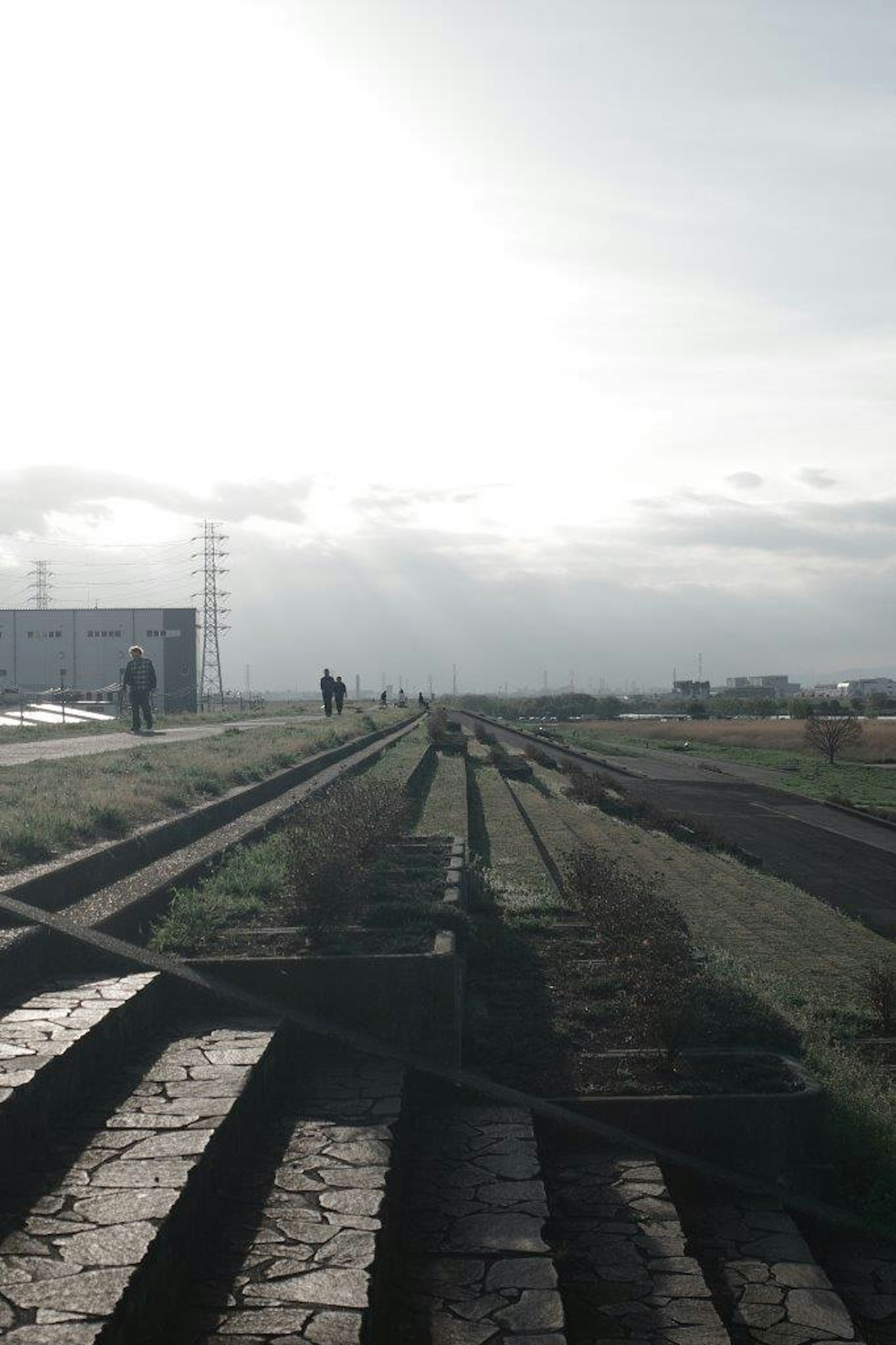 曇った空の下に広がる古い線路の風景 人々が遠くに見える