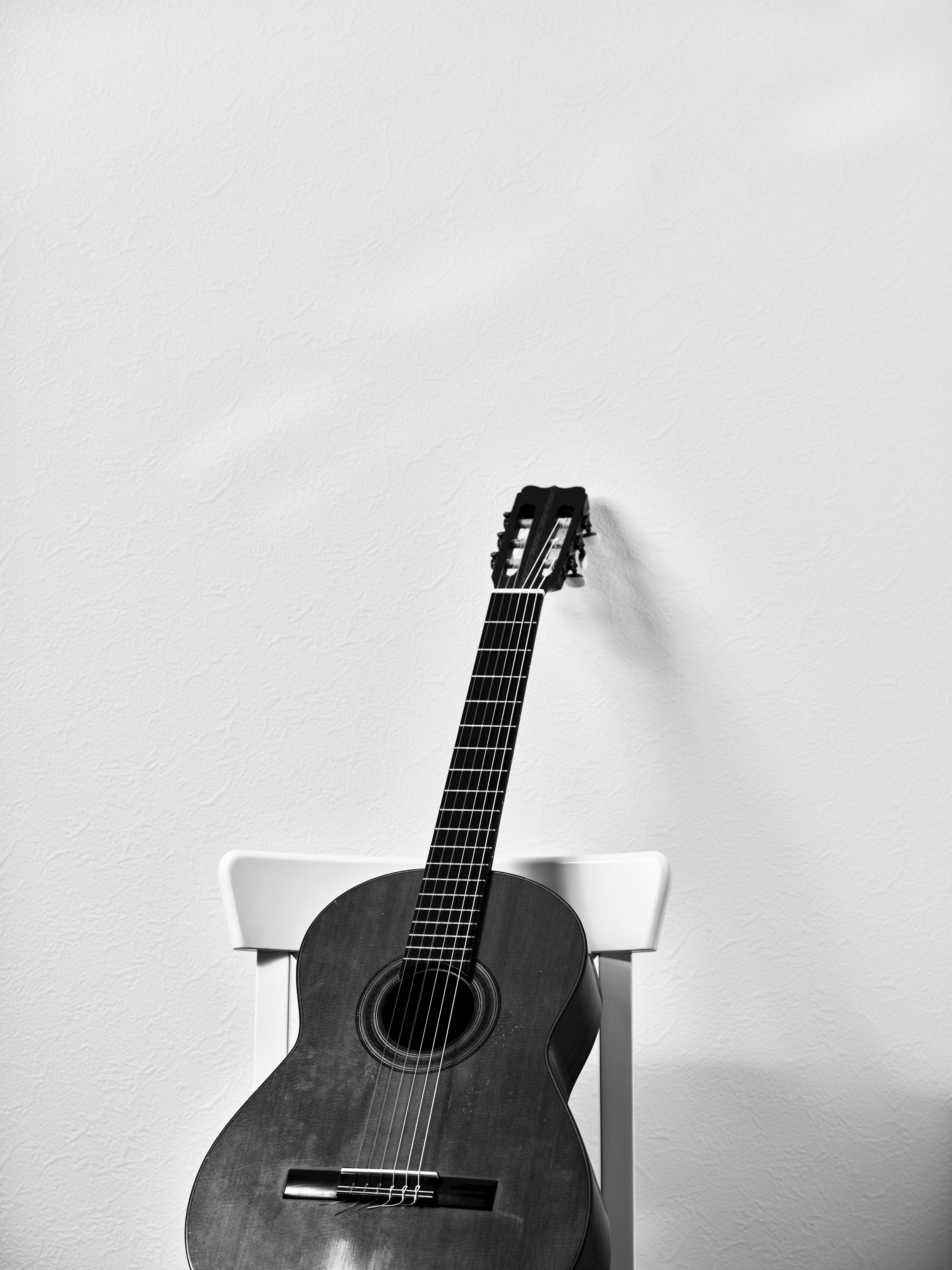 Acoustic guitar leaning against a chair in front of a white wall