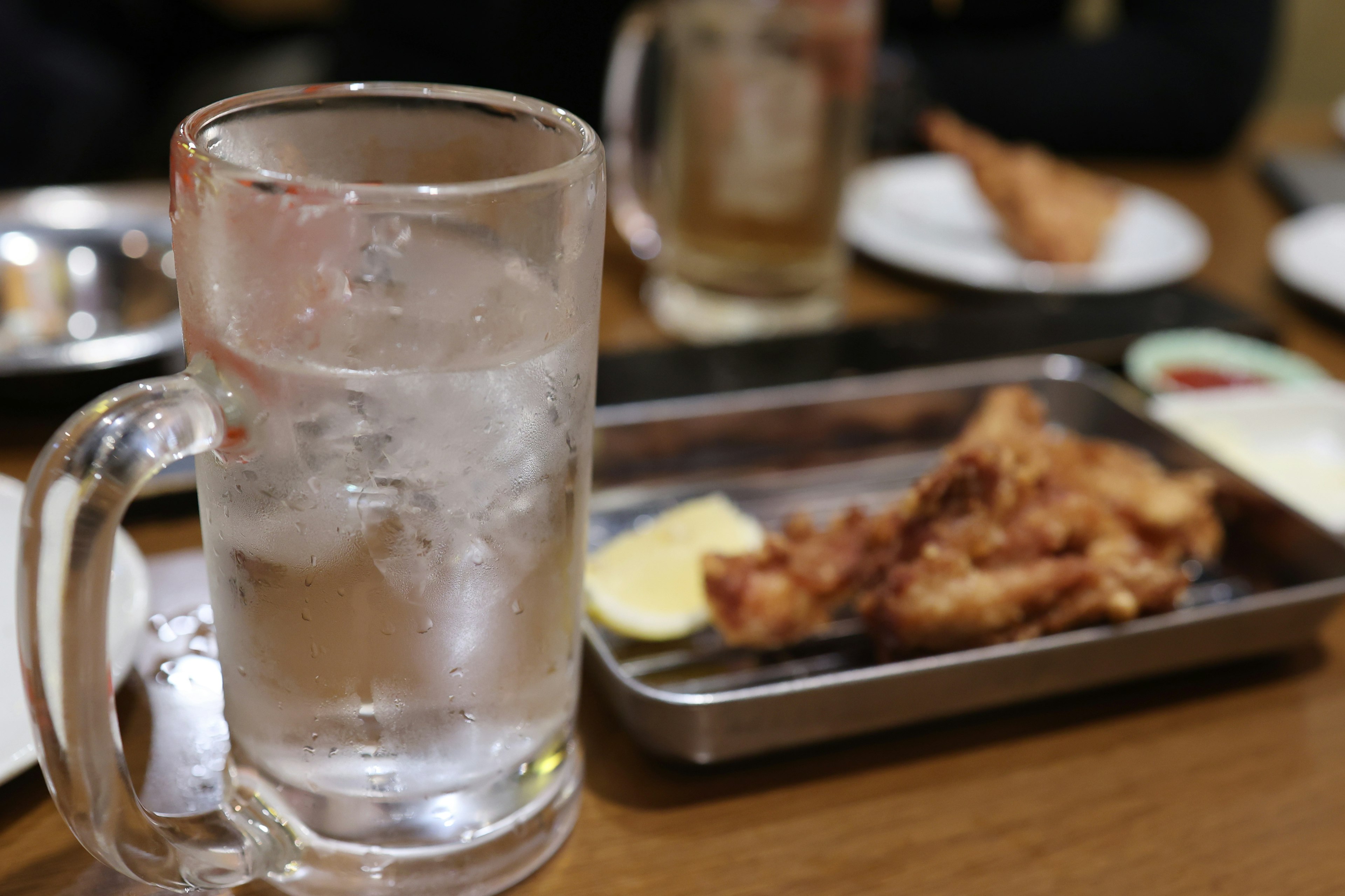 Un vaso de agua fría al lado de un plato de comida frita en una mesa de comedor