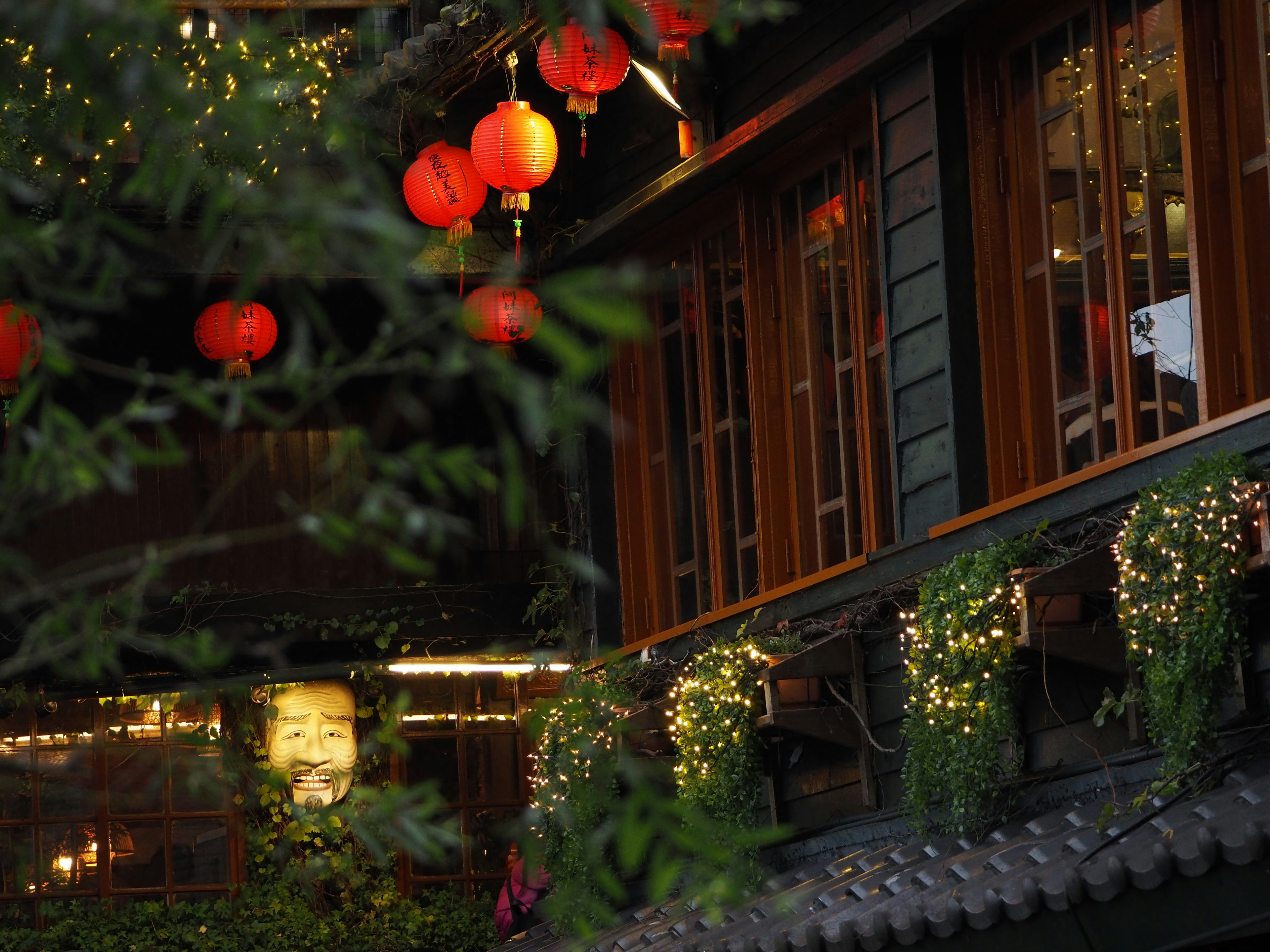 Bâtiment traditionnel avec des lanternes rouges et des plantes vertes dans un cadre nocturne