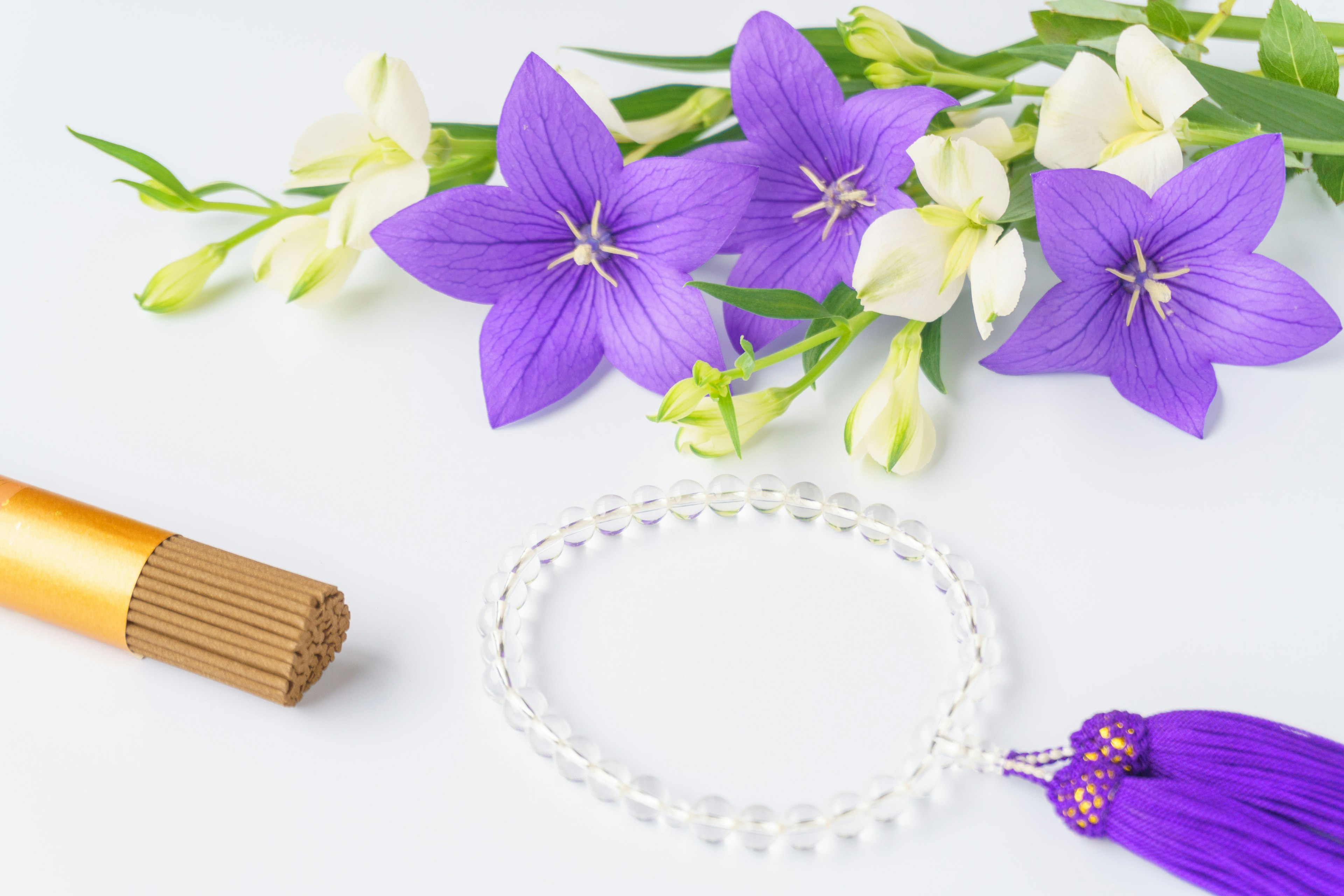 Lila und weiße Blumen schön arrangiert mit einem transparenten Perlenarmband und einem lila Quaste