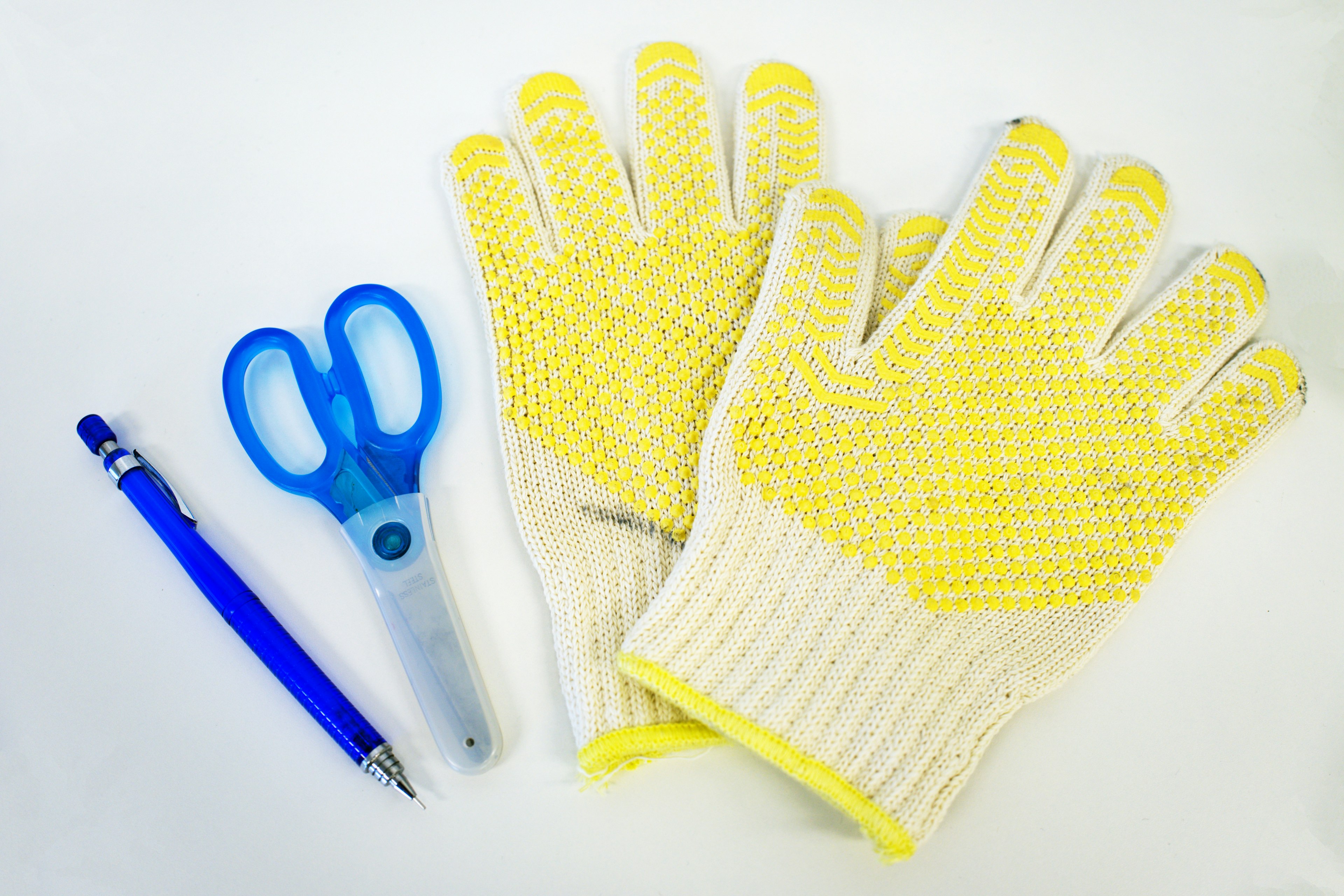 Yellow gloves with textured grip alongside blue scissors and a pen