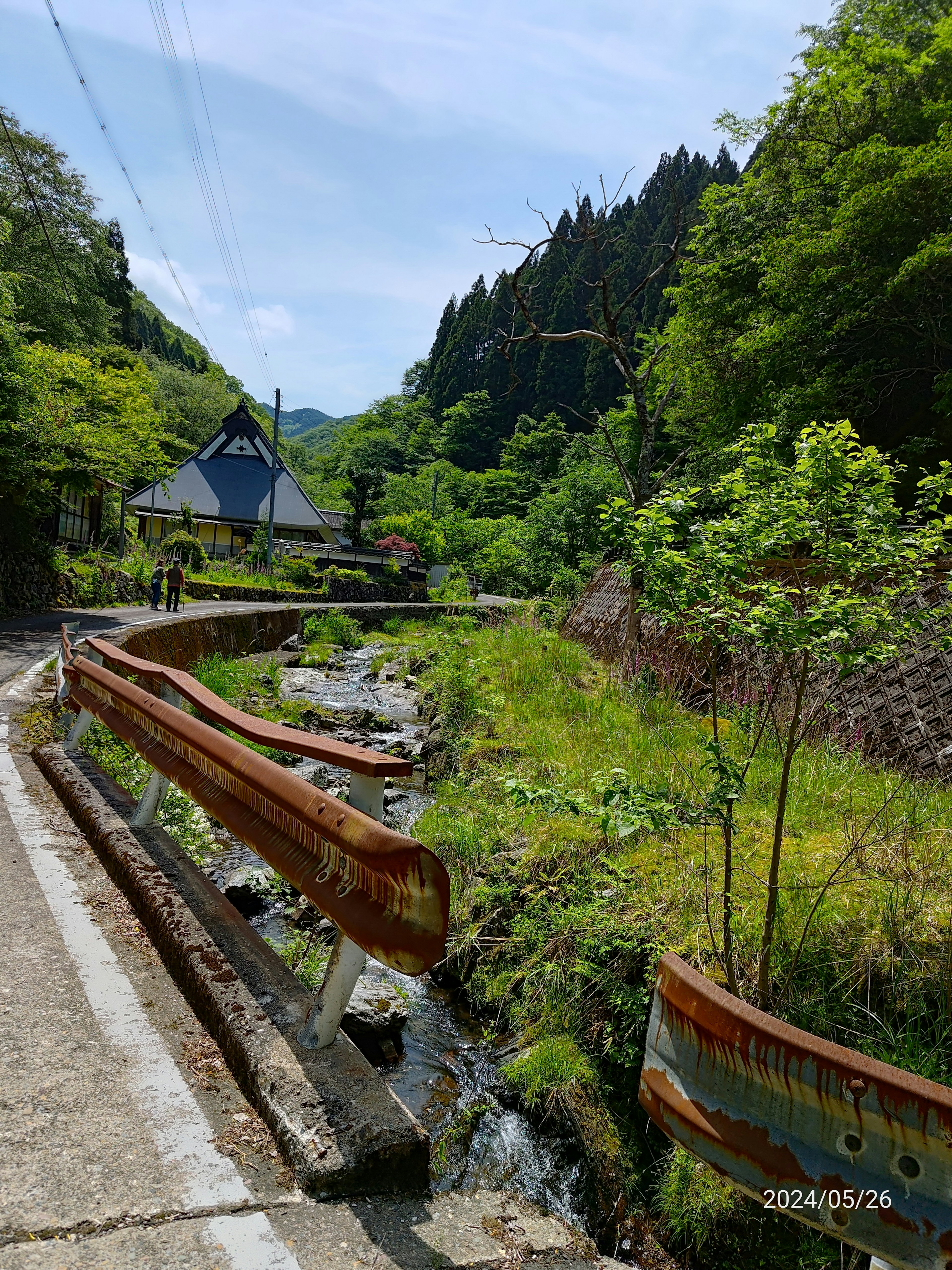 Vue pittoresque d'une route de montagne avec un ruisseau et une maison traditionnelle