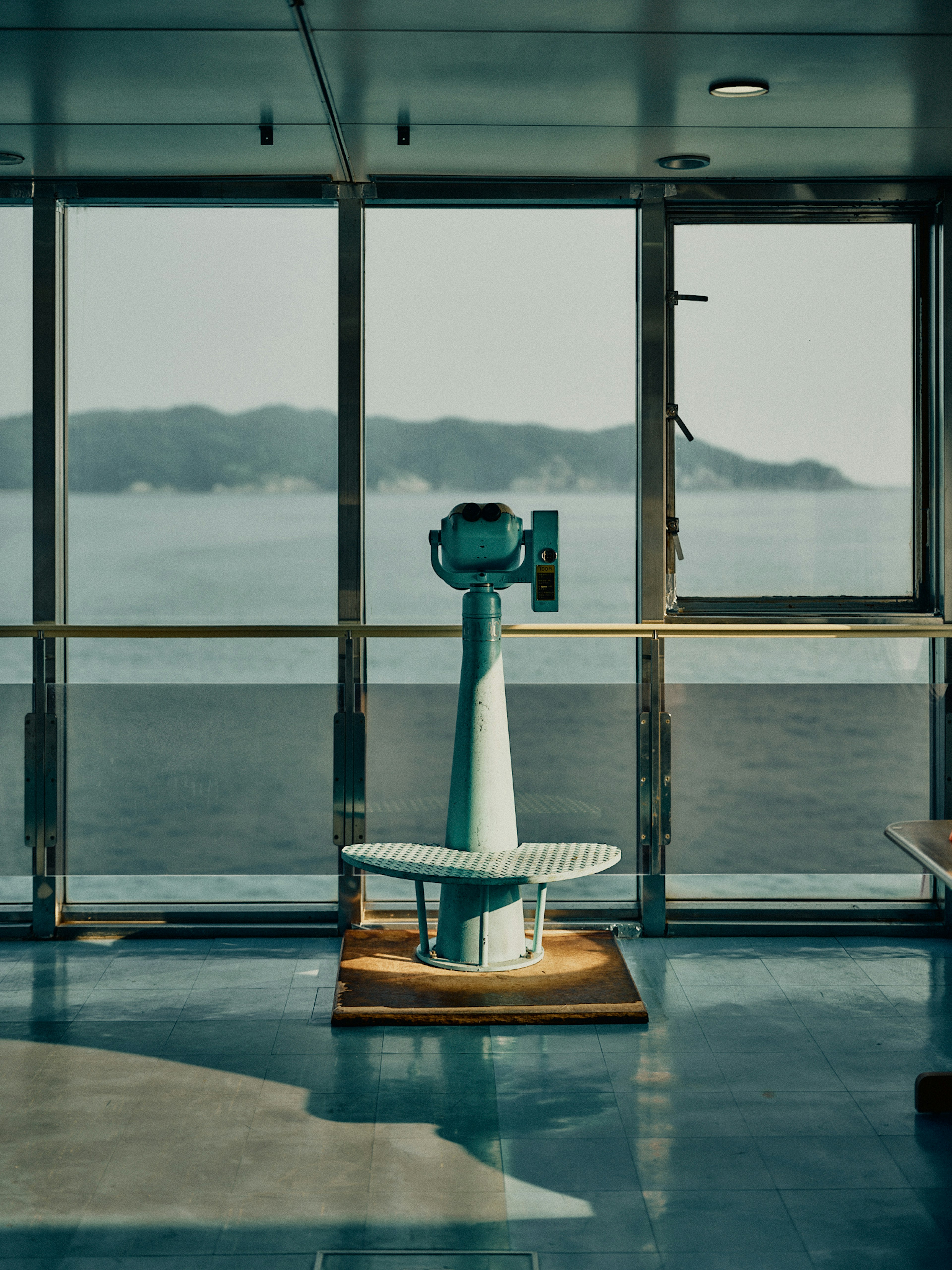 A blue telescope overlooking the sea through large windows