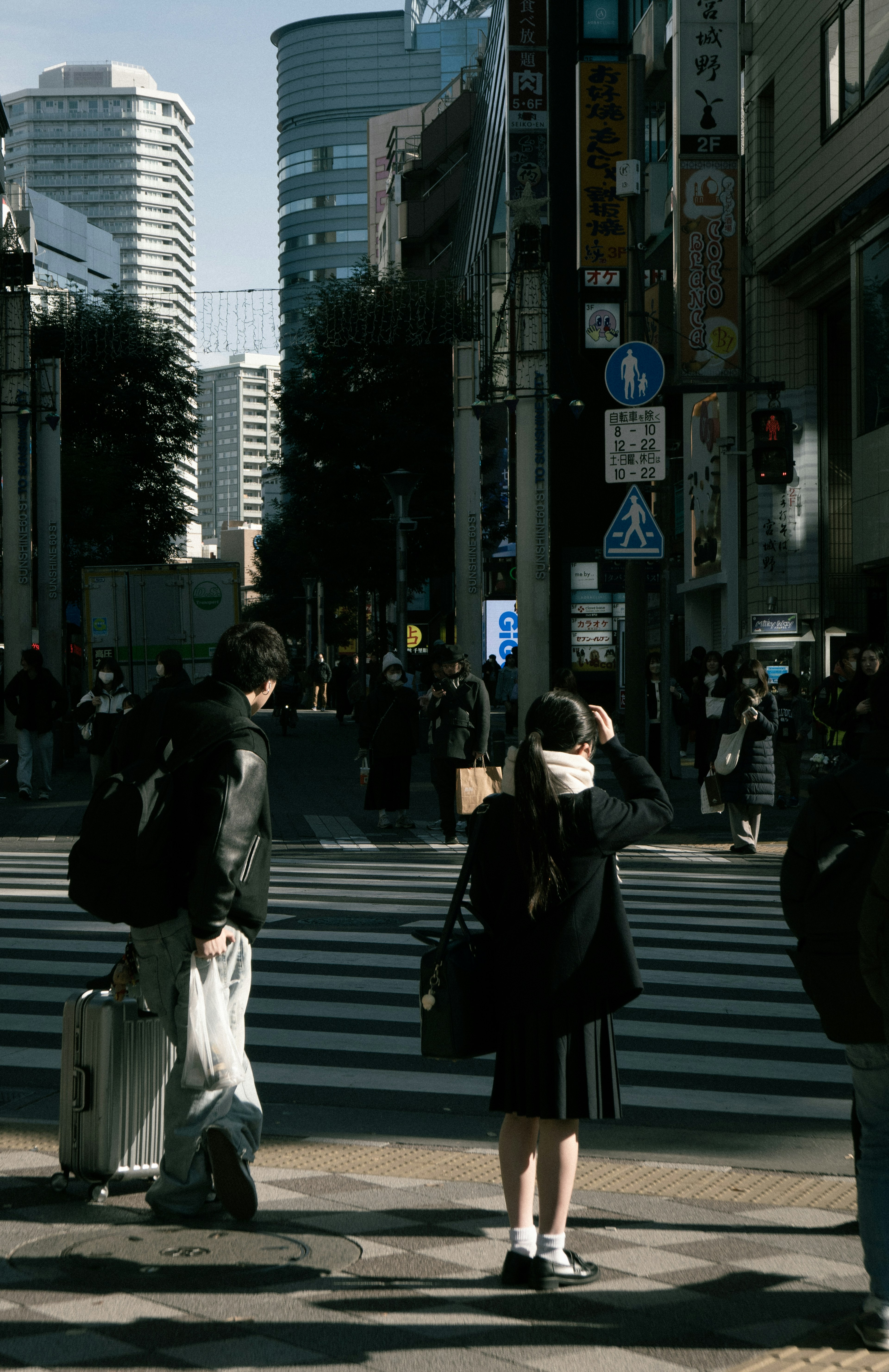 都市の交差点で信号を待つ人々とビル群