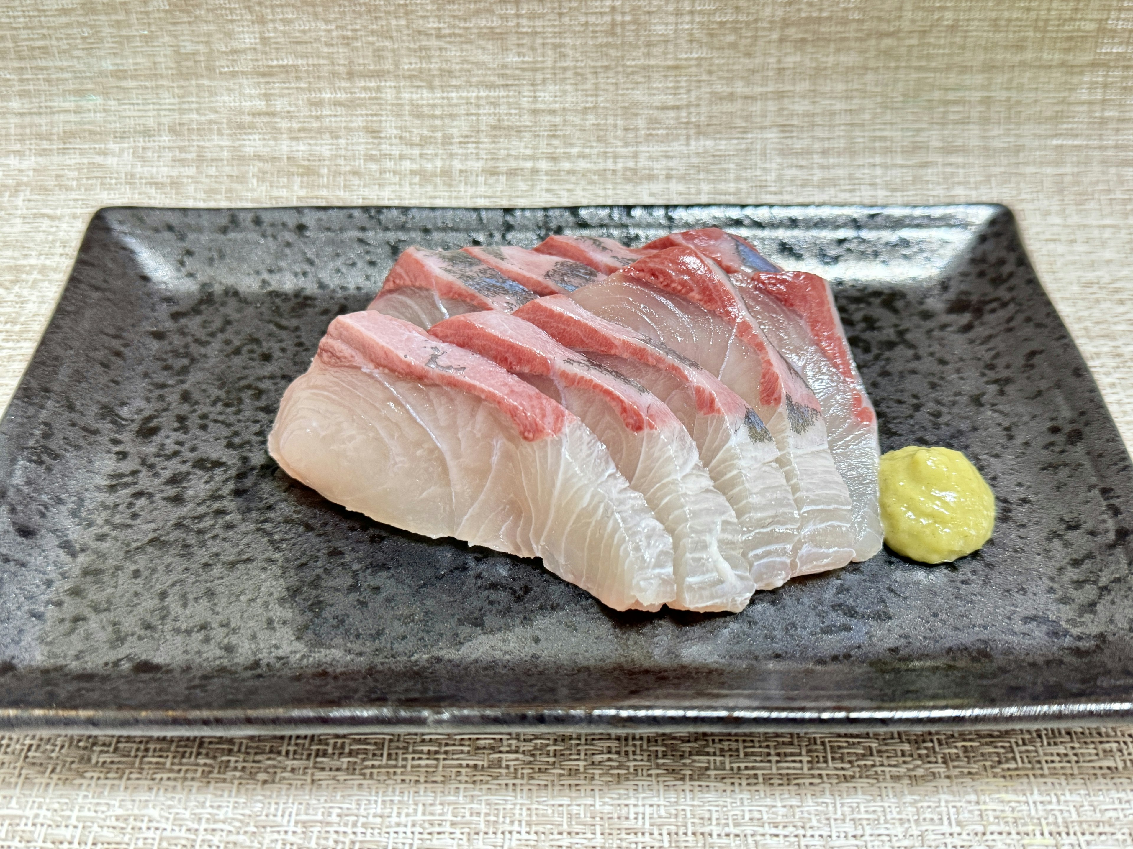 Thinly sliced fish sashimi with wasabi served on a black plate