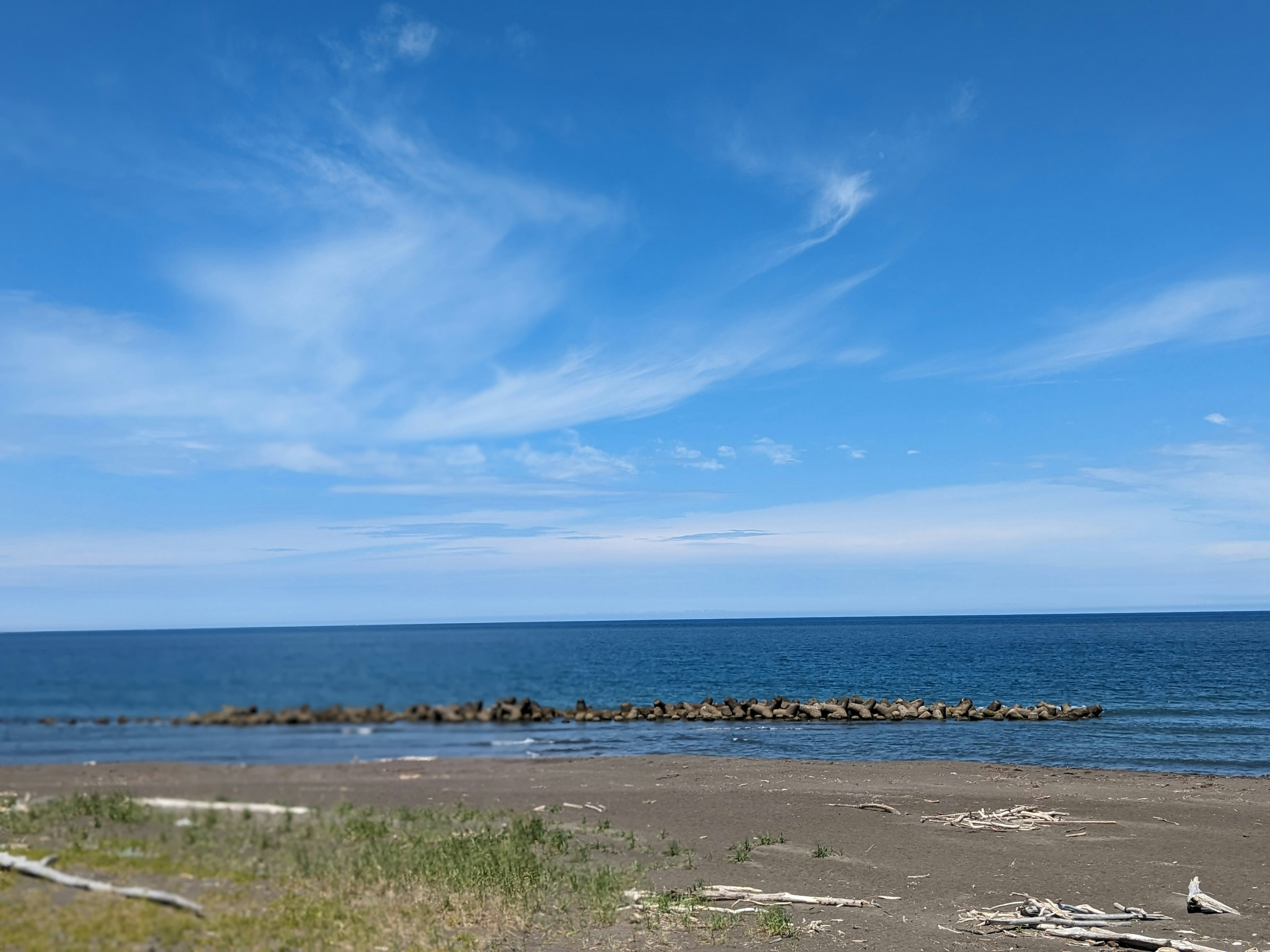 Una escena de playa con cielo azul y rocas alineadas a lo largo de la costa