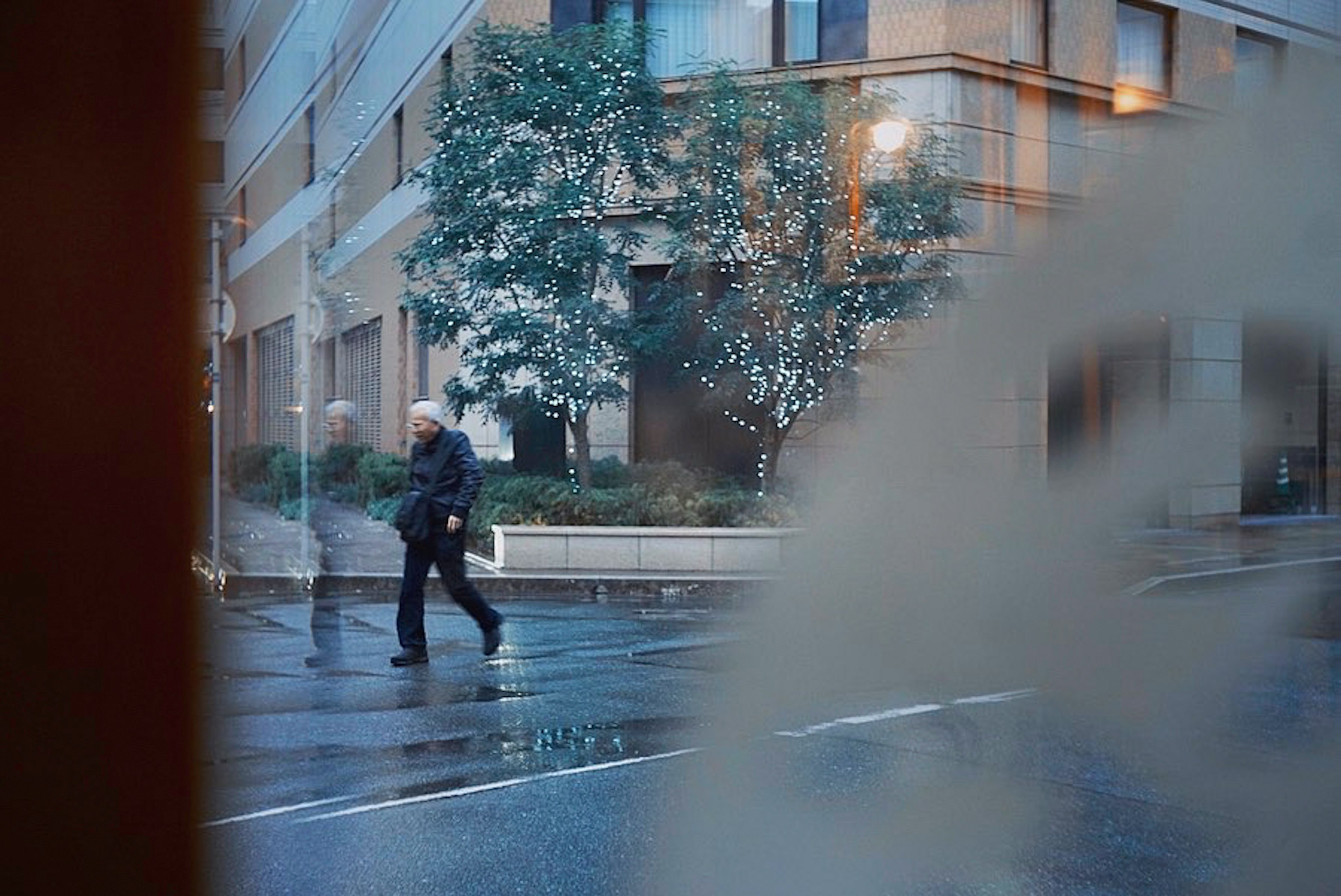 A man walking on a rainy street with trees in the background