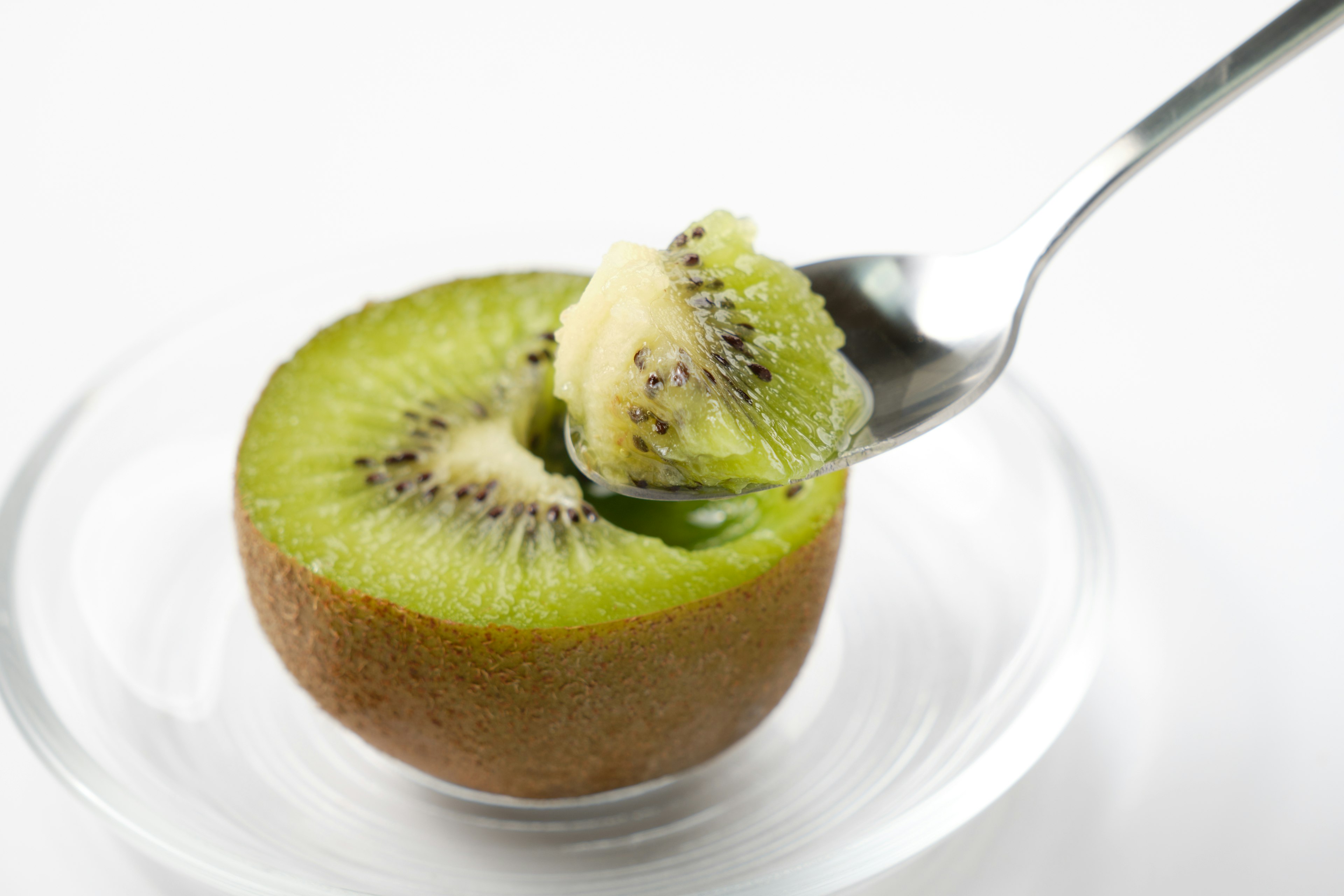 Setengah buah kiwi di piring dengan sendok yang mengambil daging buah