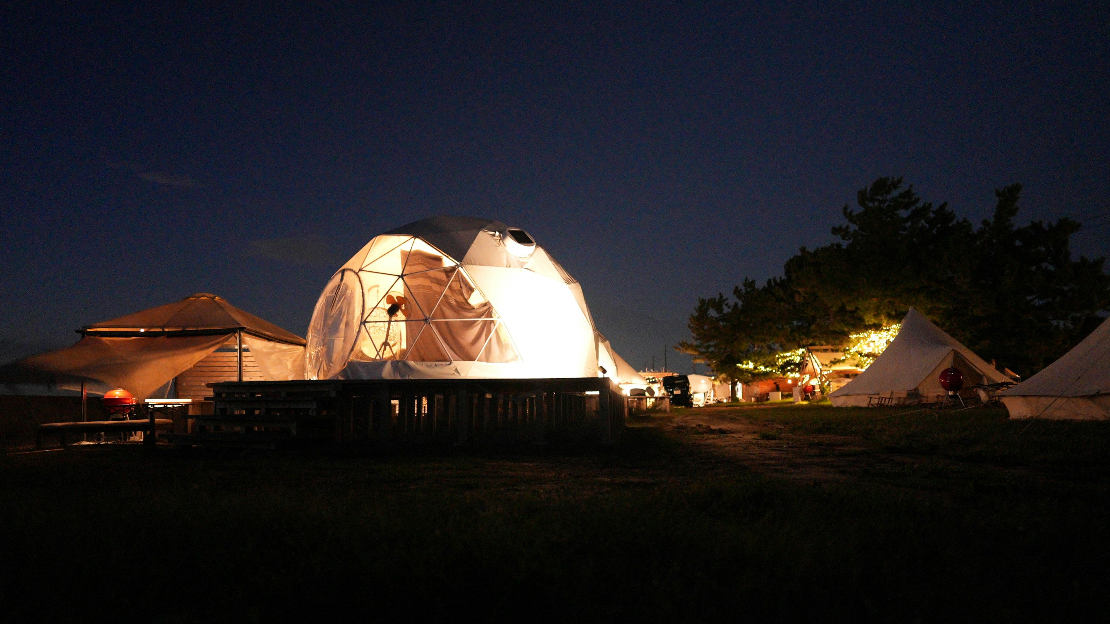 Kamp malam dengan tenda dome dan tenda yang diterangi