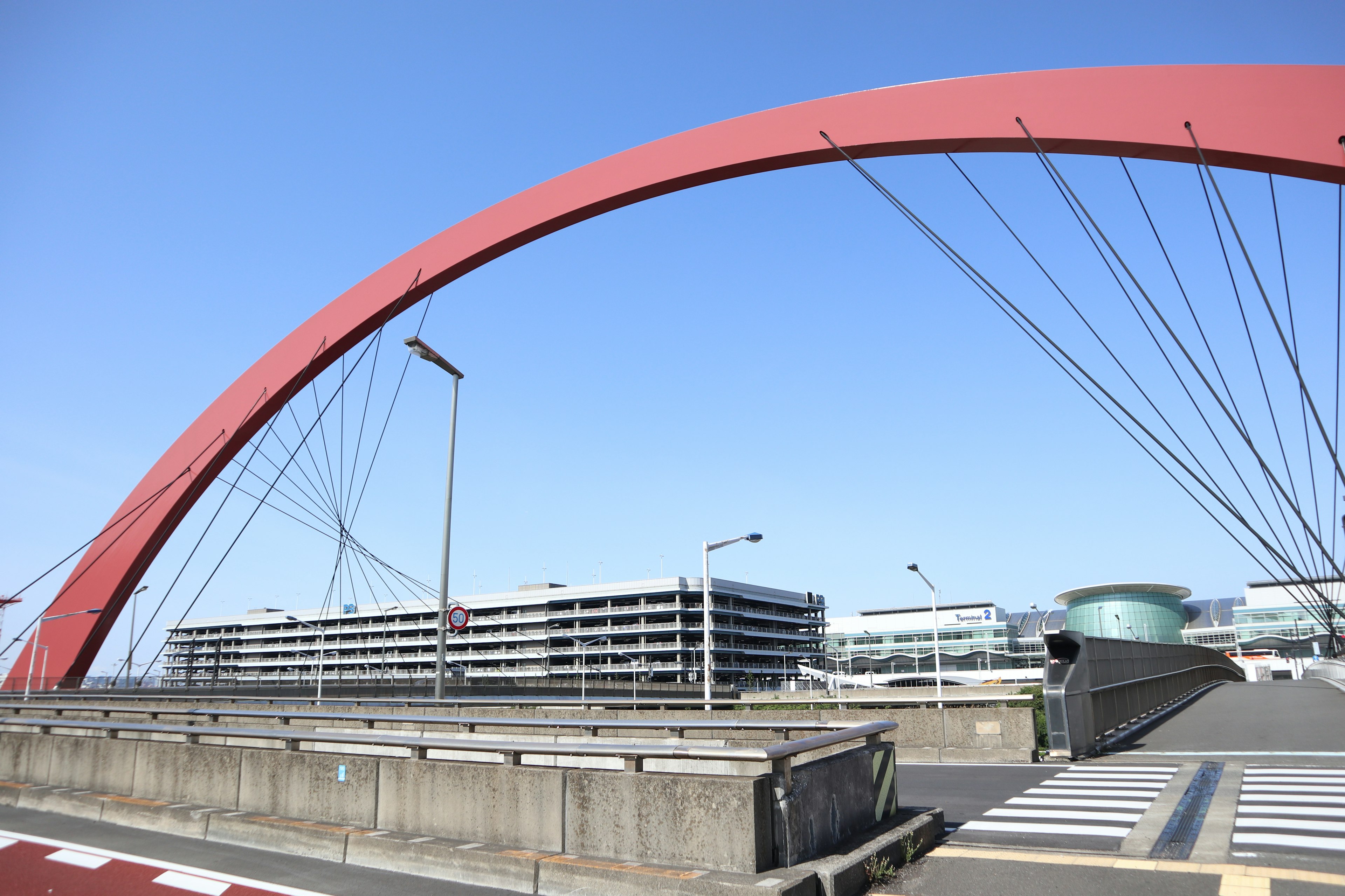 Red arch bridge under a clear blue sky with modern buildings nearby