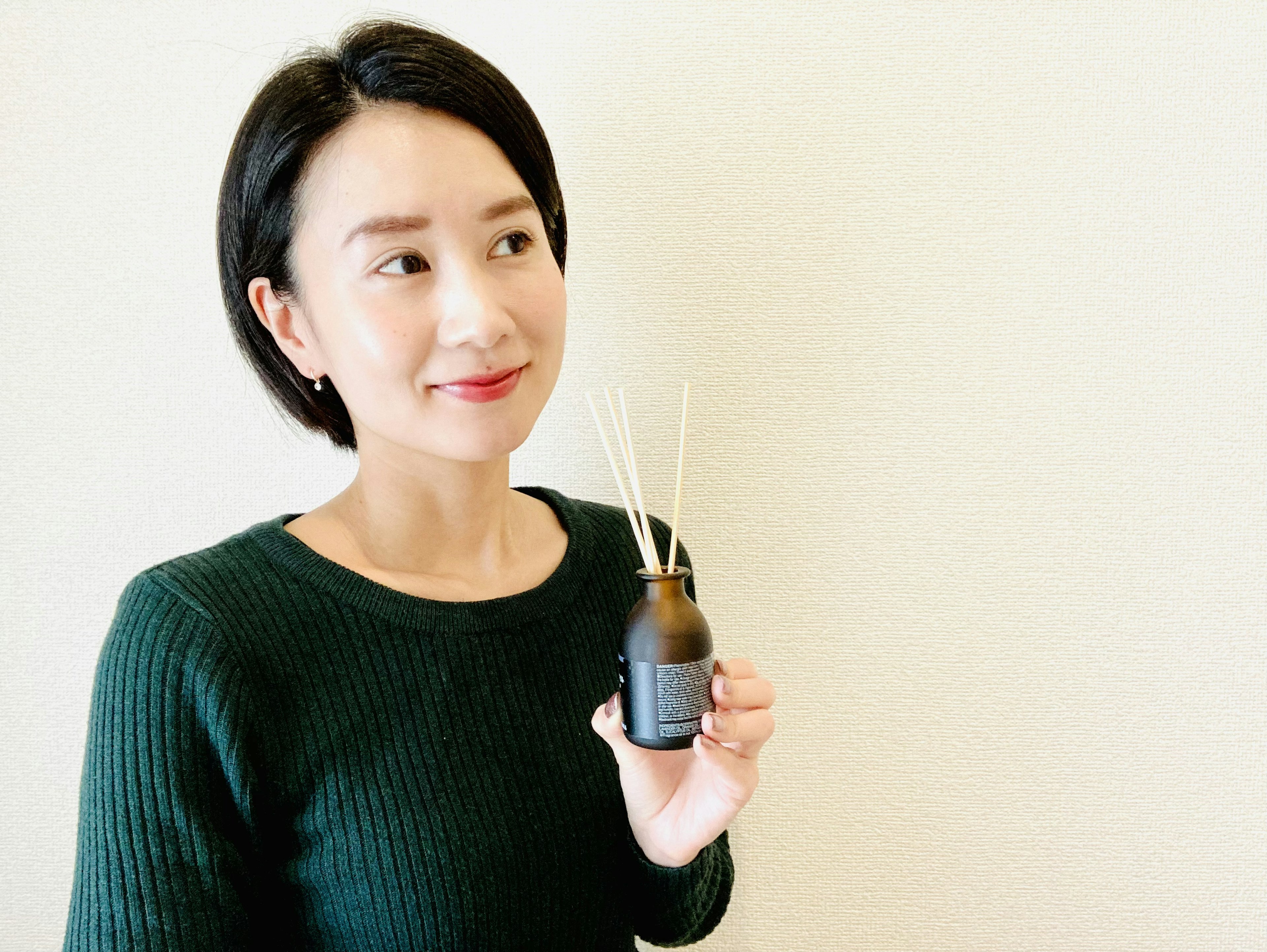 Woman smiling while holding a fragrance diffuser with sticks