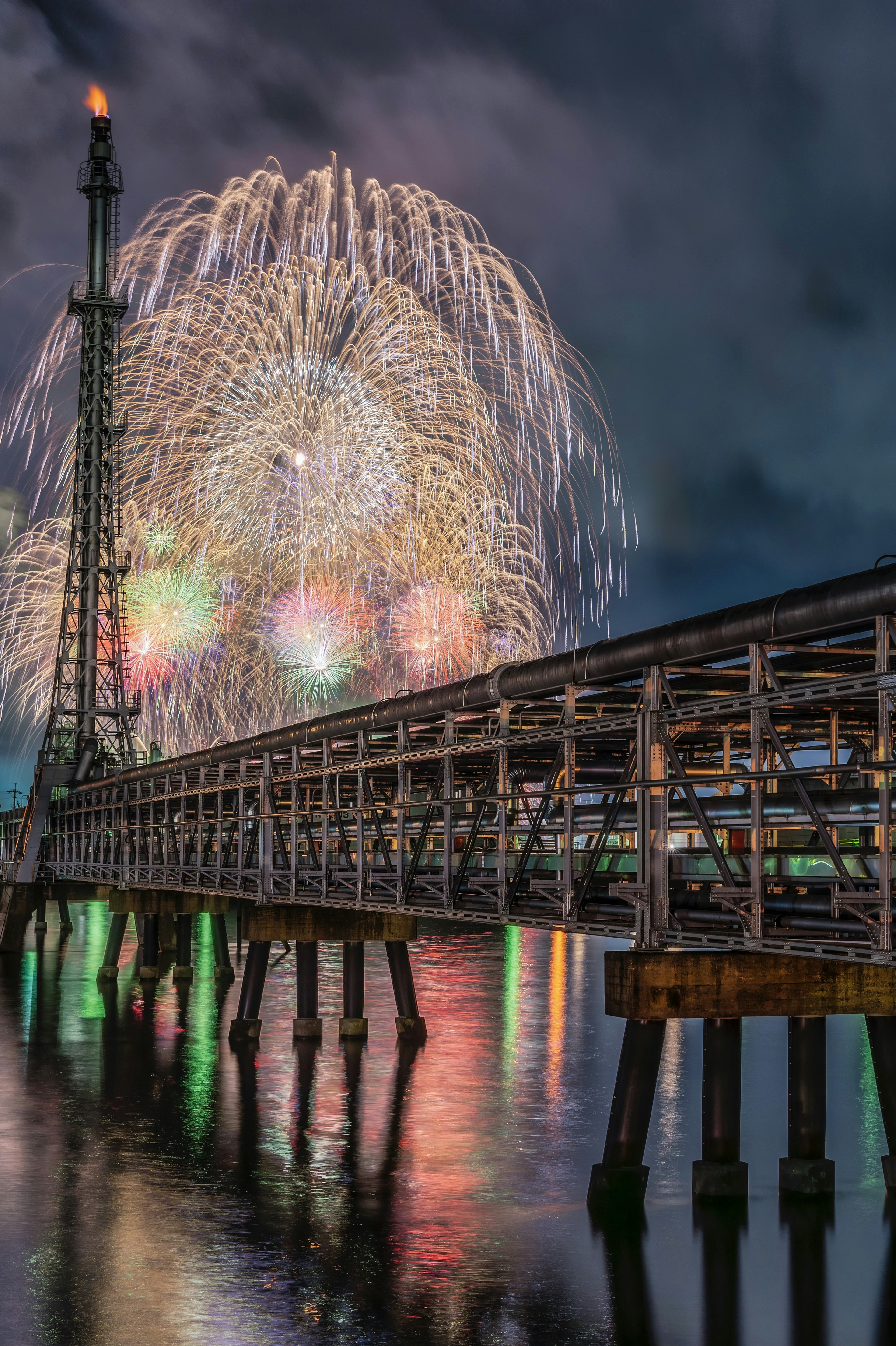 Una hermosa escena de fuegos artificiales estallando en el cielo nocturno con un muelle reflejándose en el agua