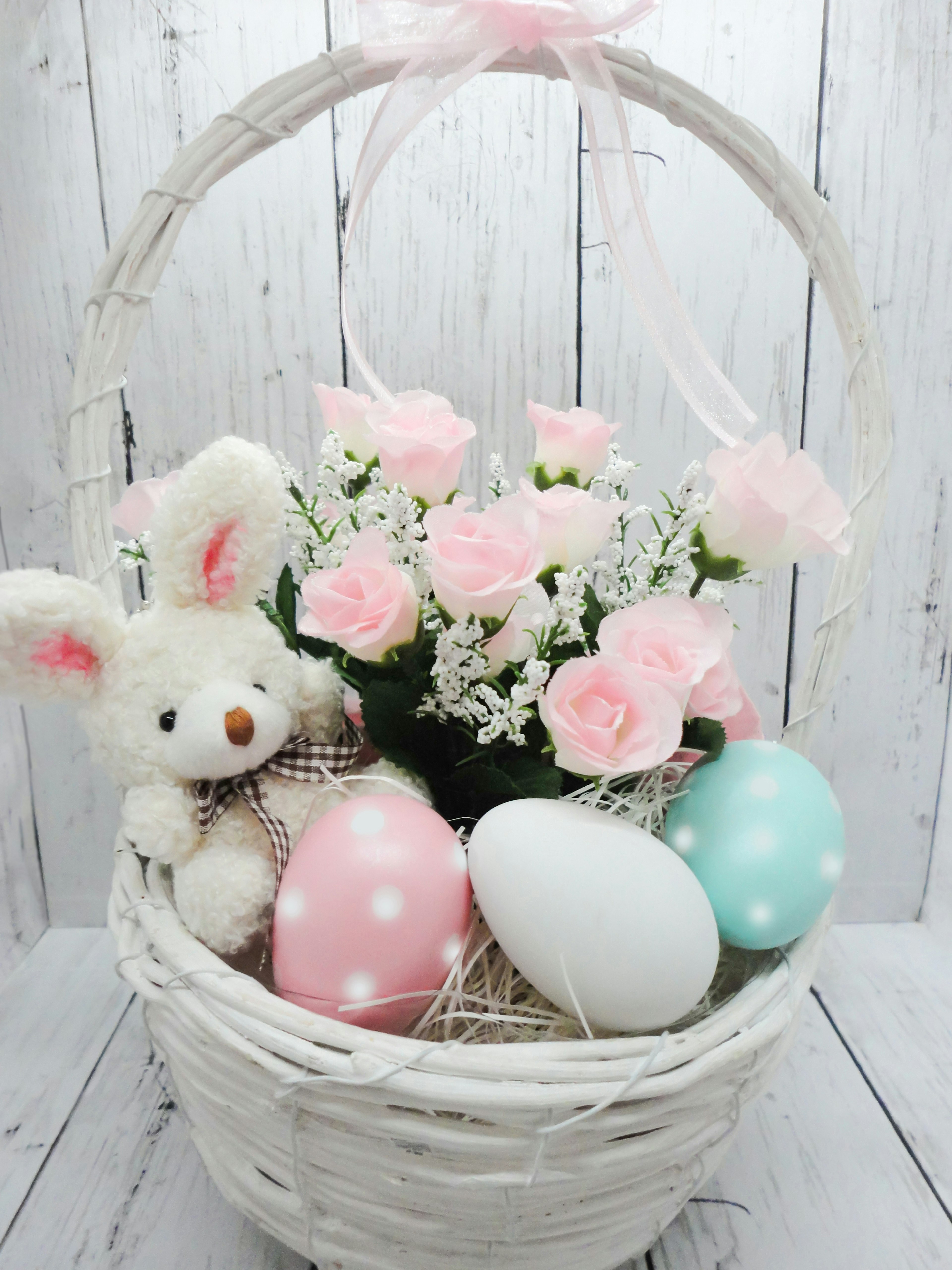 Un panier blanc contenant des fleurs roses et des œufs colorés