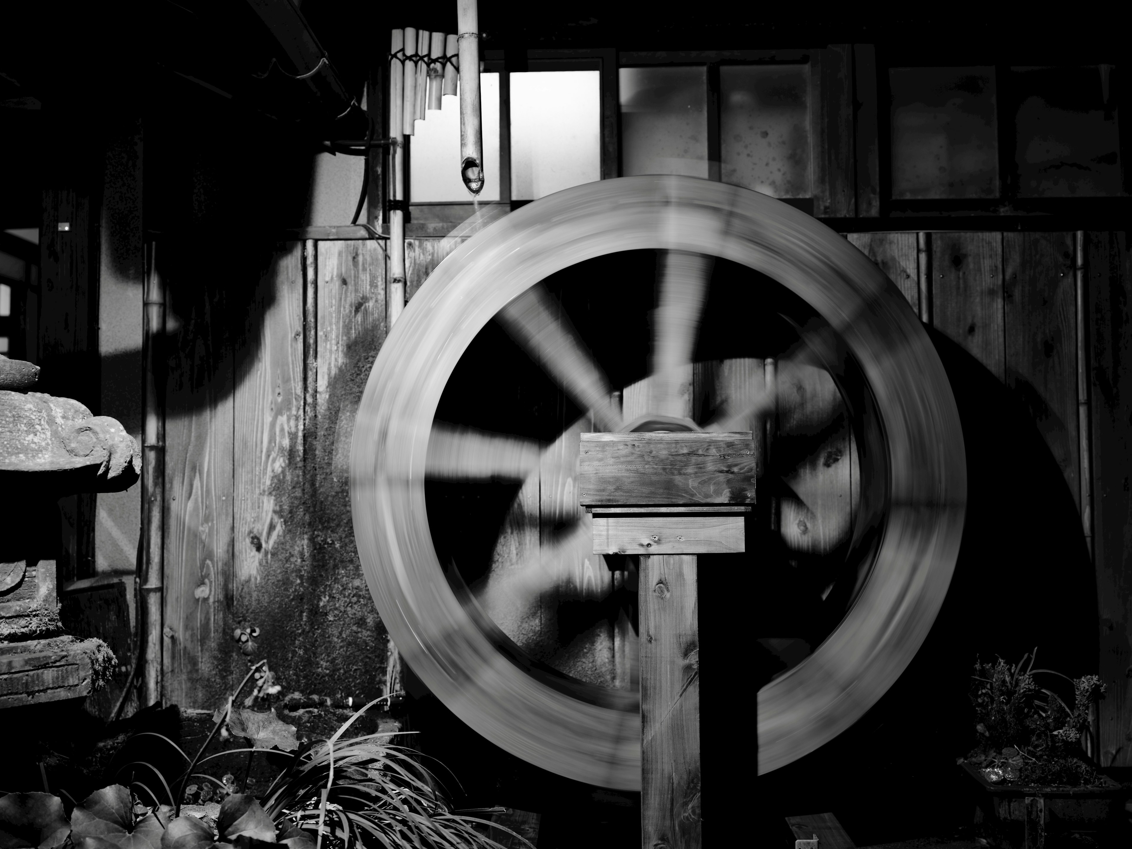 Black and white photo of a spinning waterwheel with a wooden structure and serene background