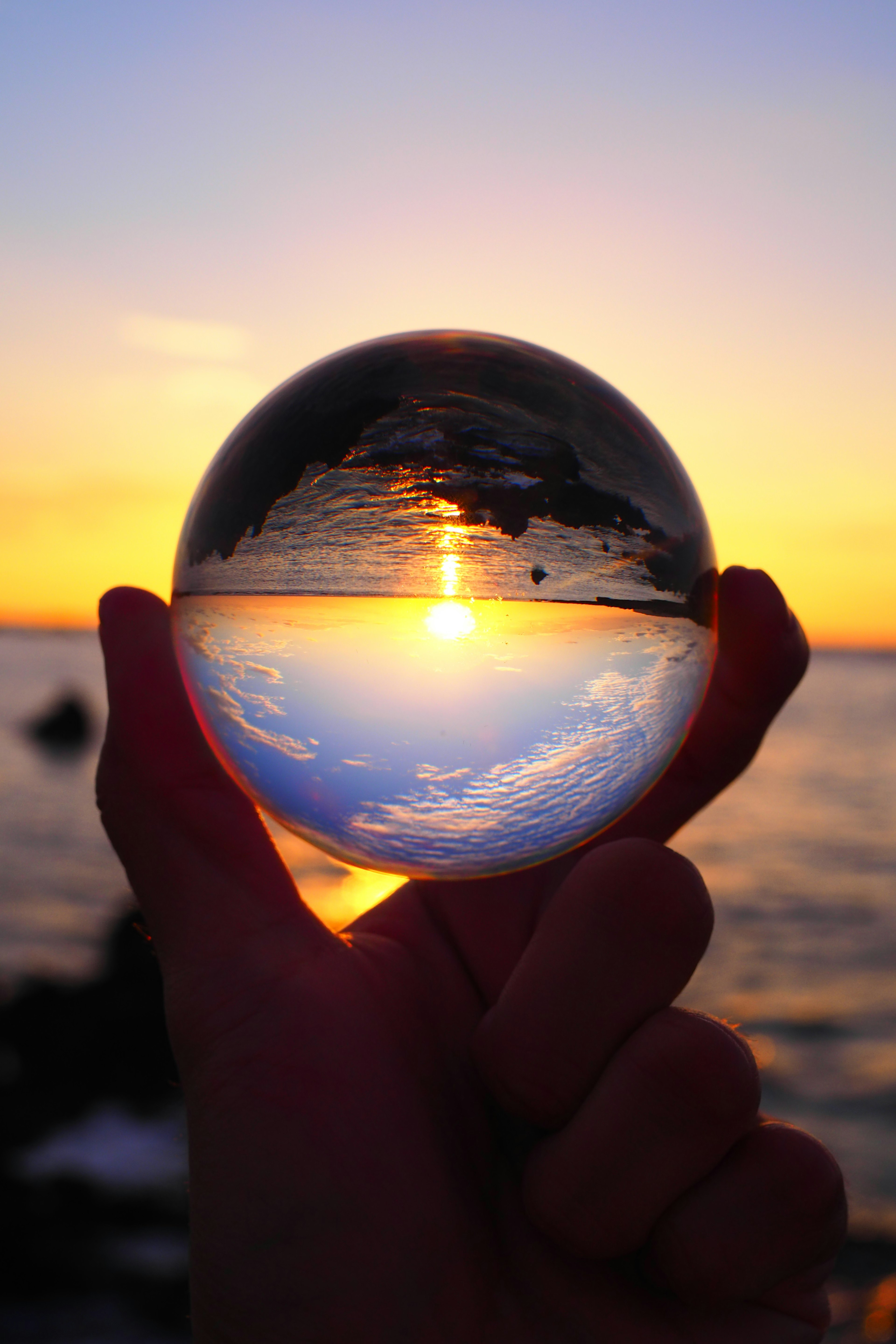 A crystal ball held in hand reflecting a sunset and ocean view