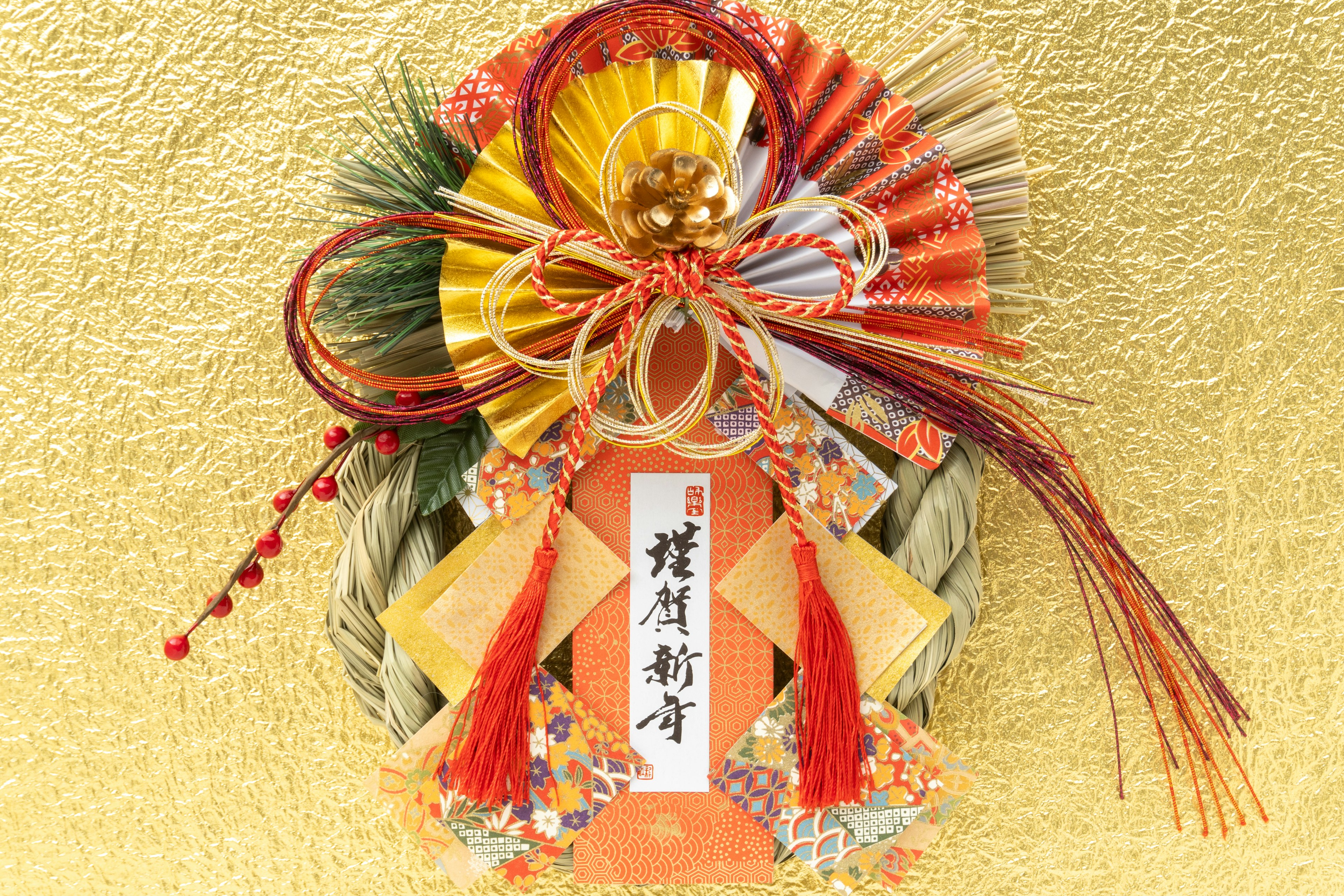 Japanese New Year decoration featuring a colorful shimekazari with ribbons and pine leaves against a golden background