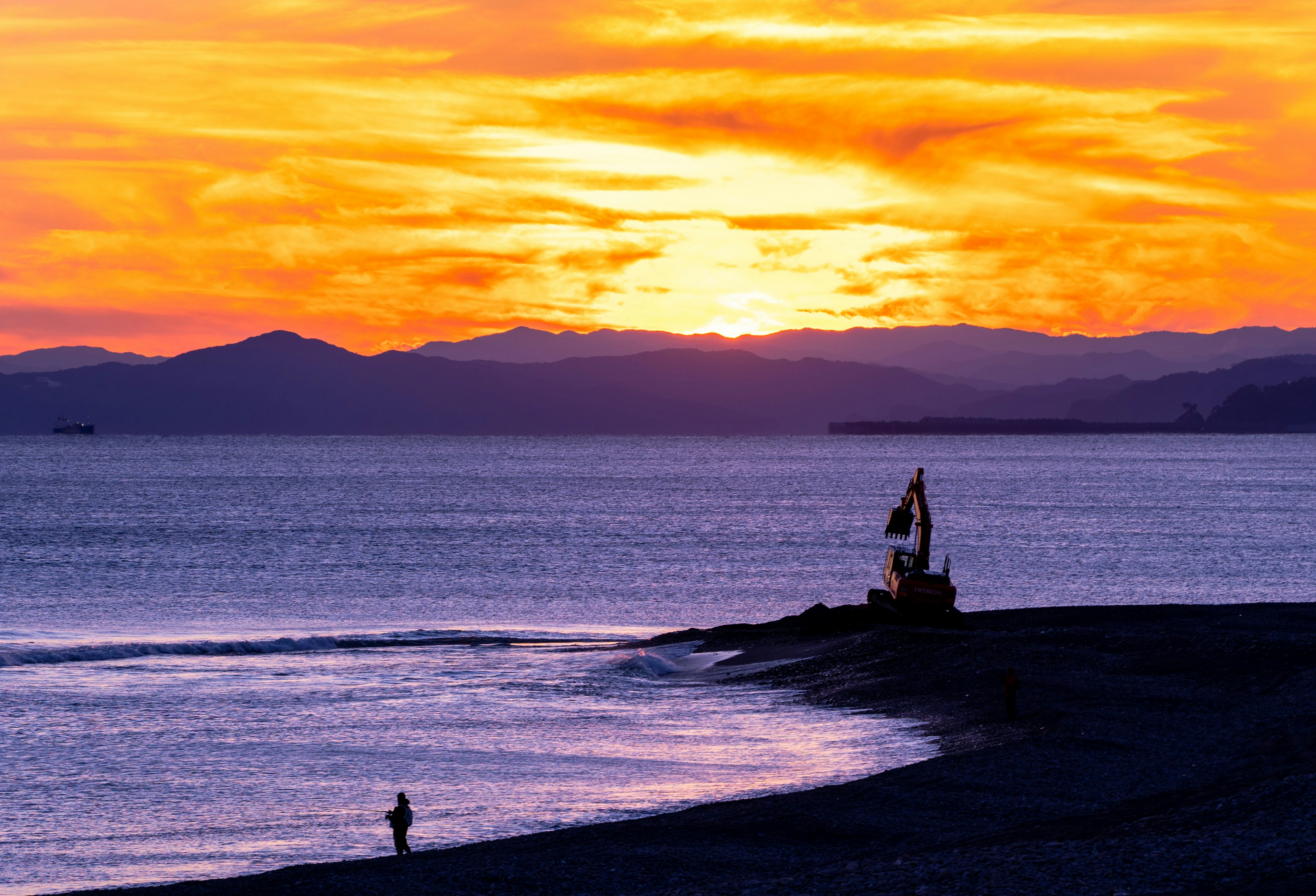 Incantevole tramonto sull'oceano con la silhouette di un peschereccio e una persona sulla spiaggia