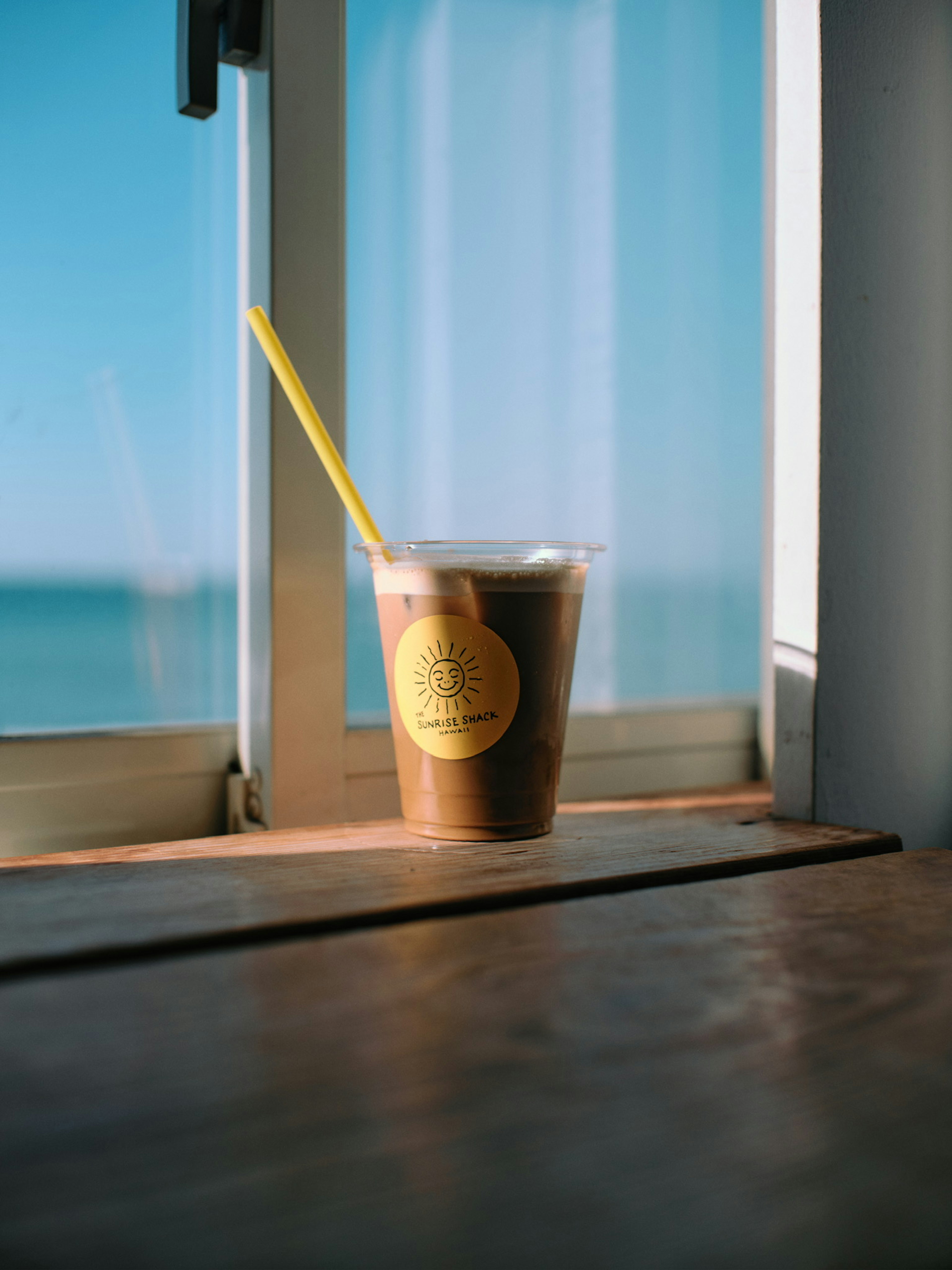 窓辺に置かれたアイスコーヒーのカップと青い海の背景