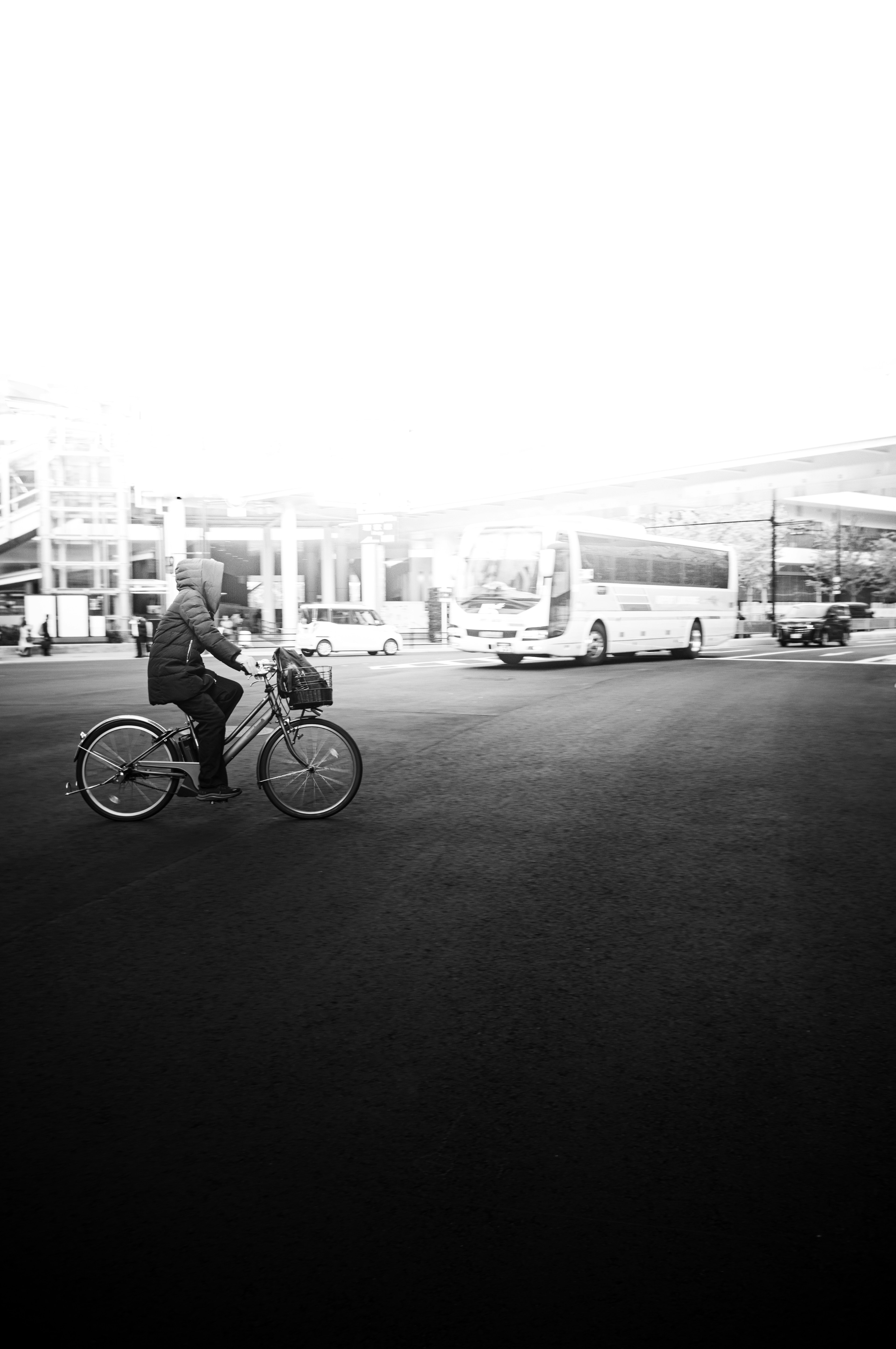 Black and white photo featuring a person on a bicycle with buses in the background