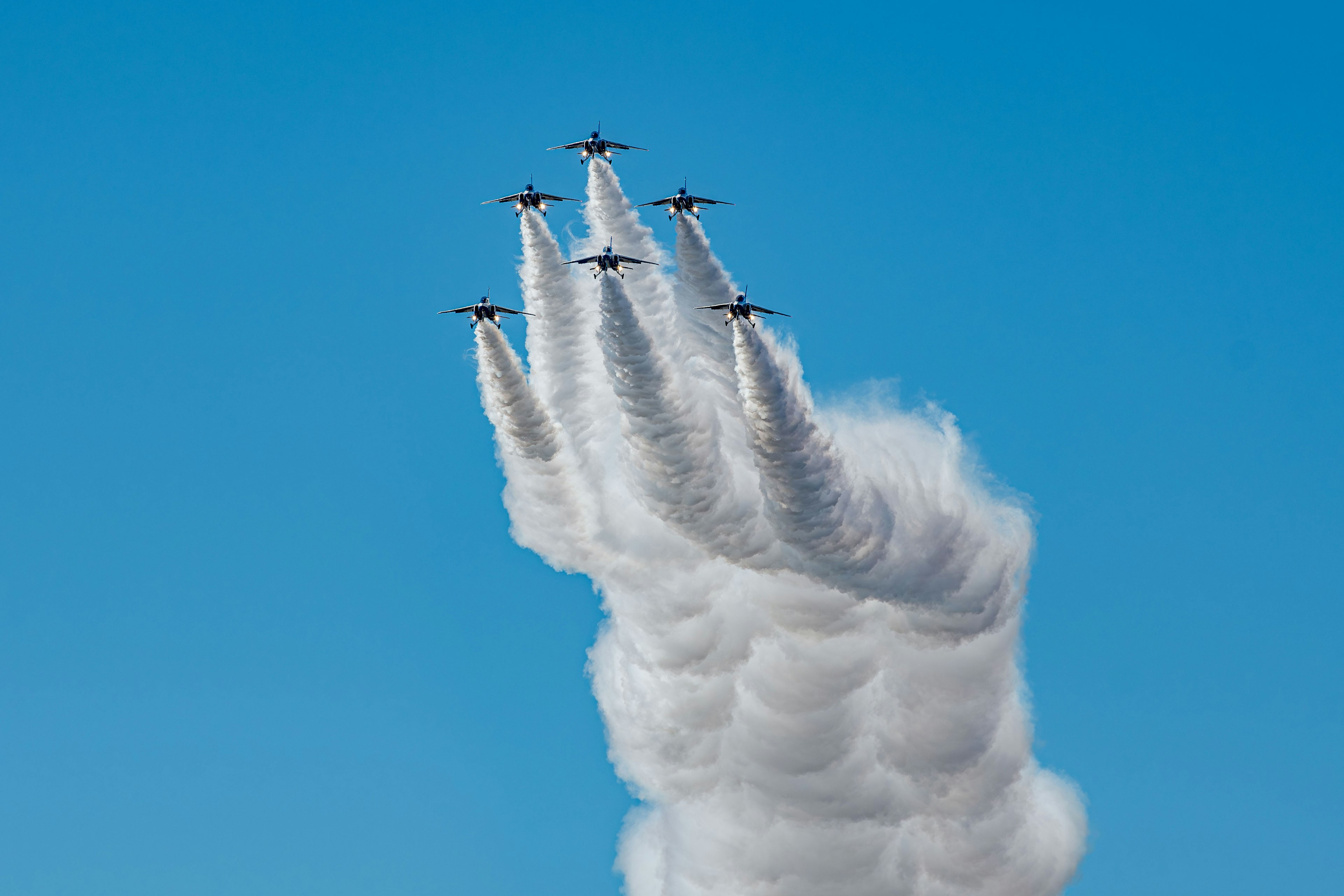 Formación de aviones ascendiendo con humo blanco contra un cielo azul