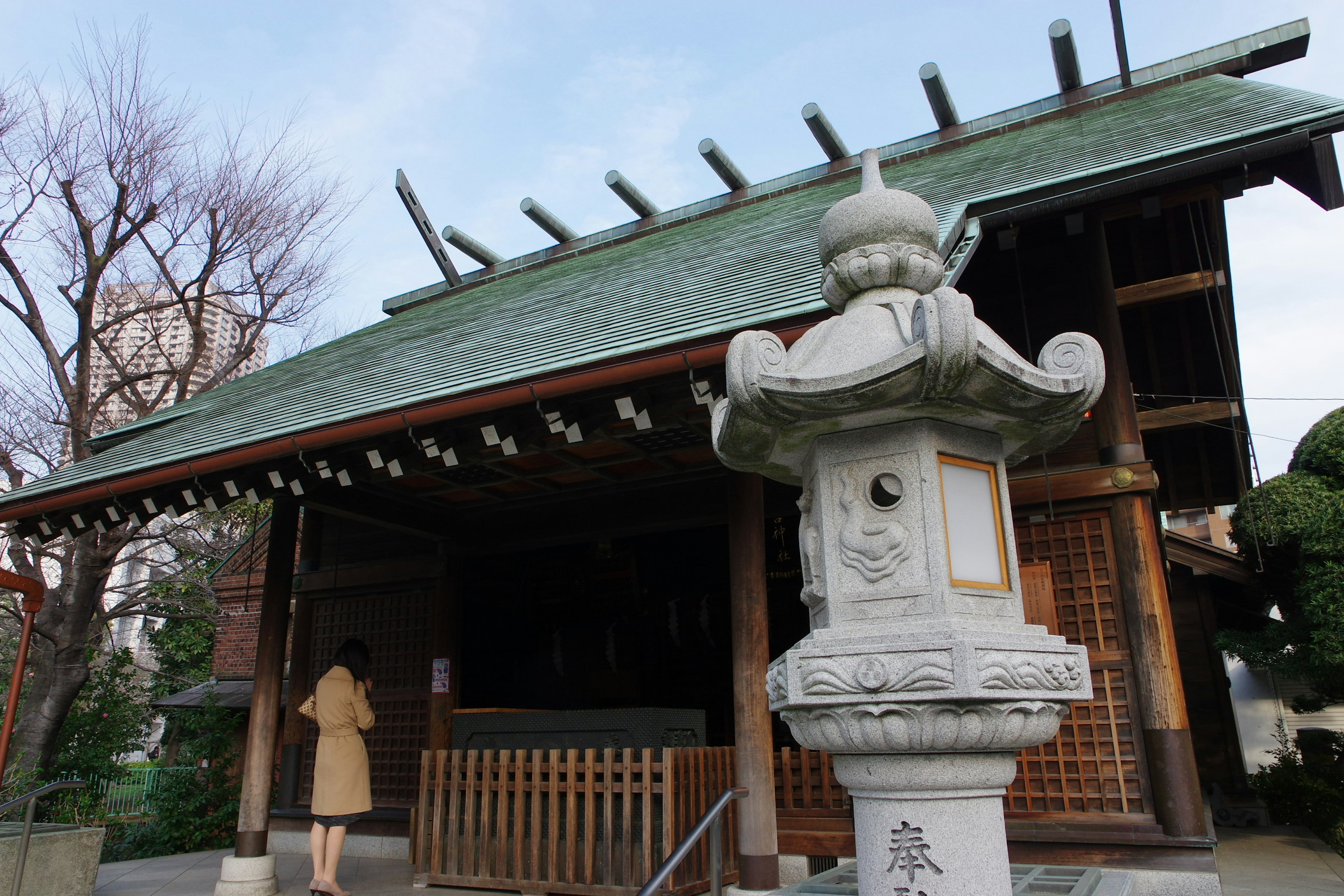 Traditional shrine building with a stone lantern visible A woman is approaching the shrine