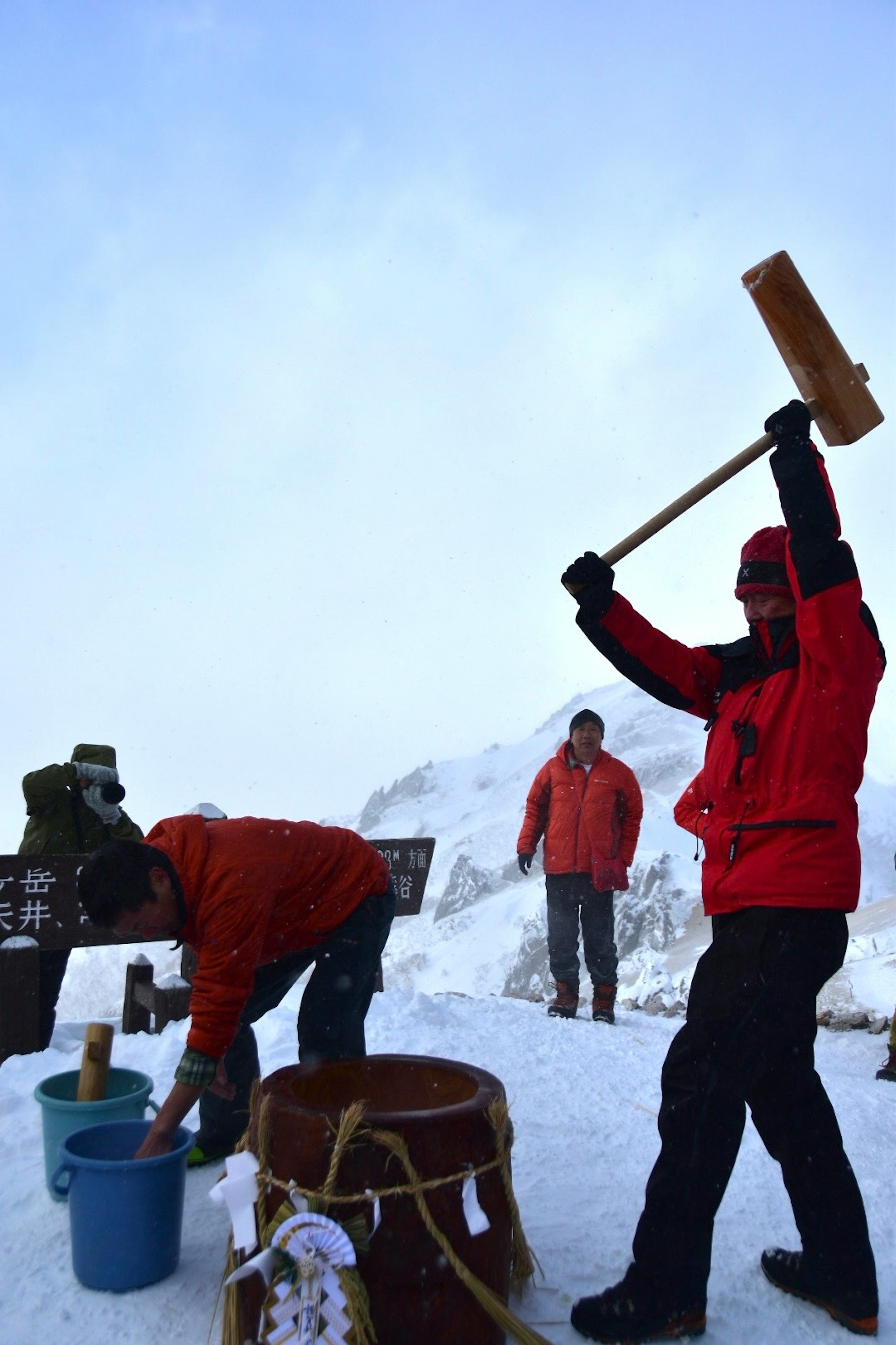 Scène de personnes travaillant sur une montagne enneigée avec un homme en vêtements rouges levant un maillet en bois