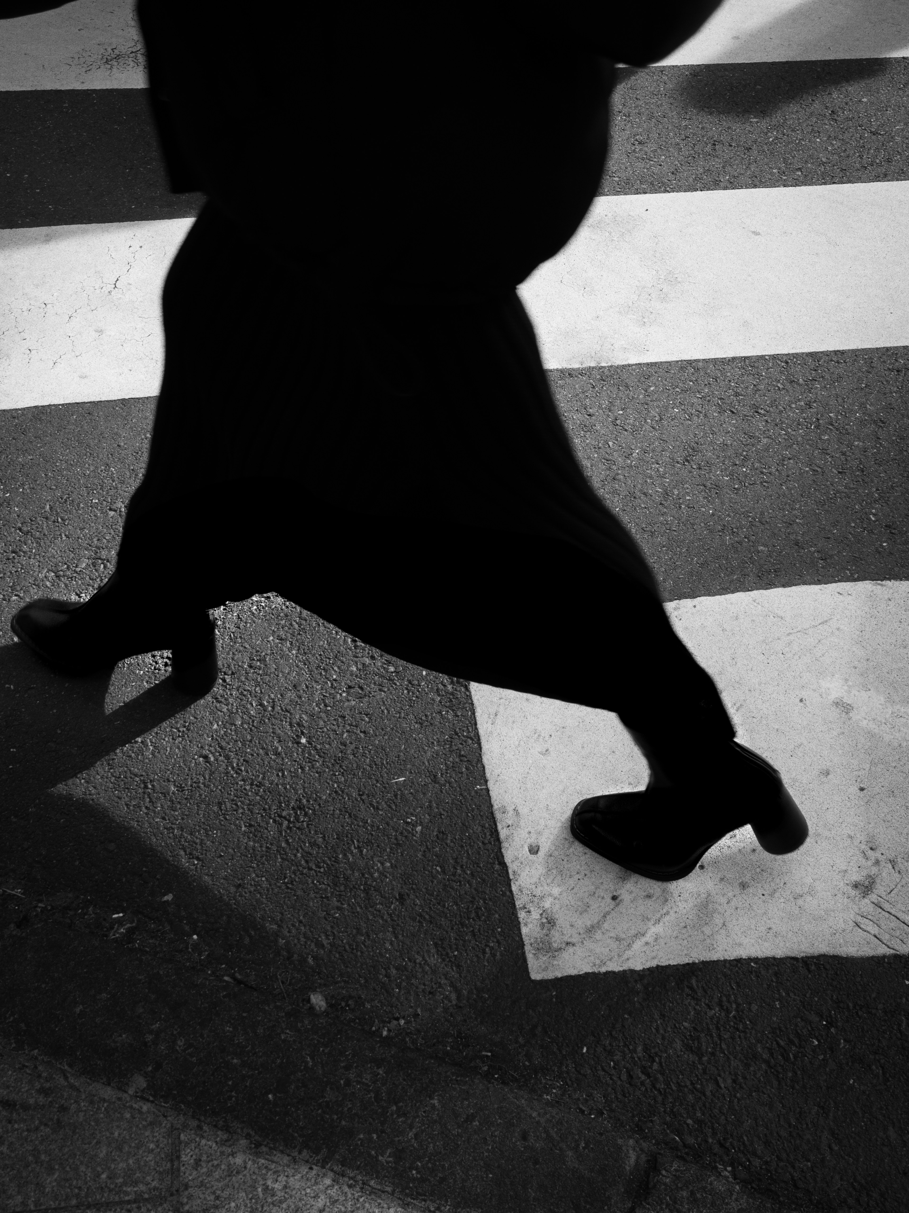 Ombra di una donna che cammina su un attraversamento pedonale con scarpe nere