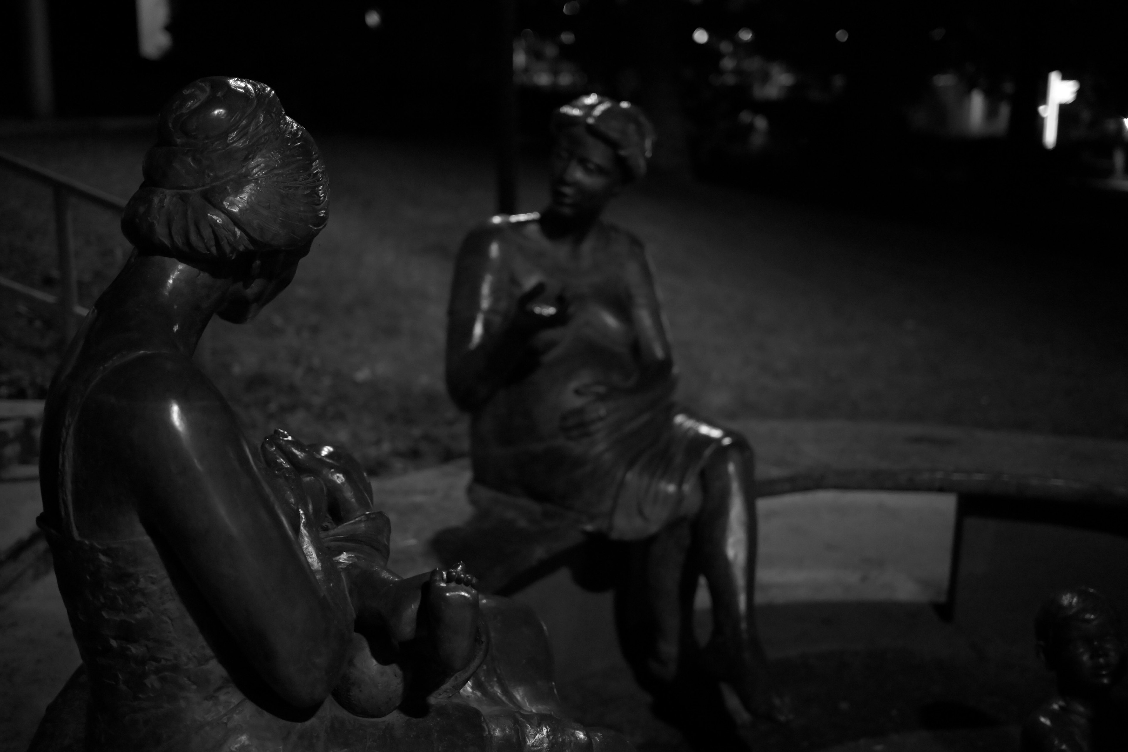 Dos estatuas de bronce sentadas en un parque de noche