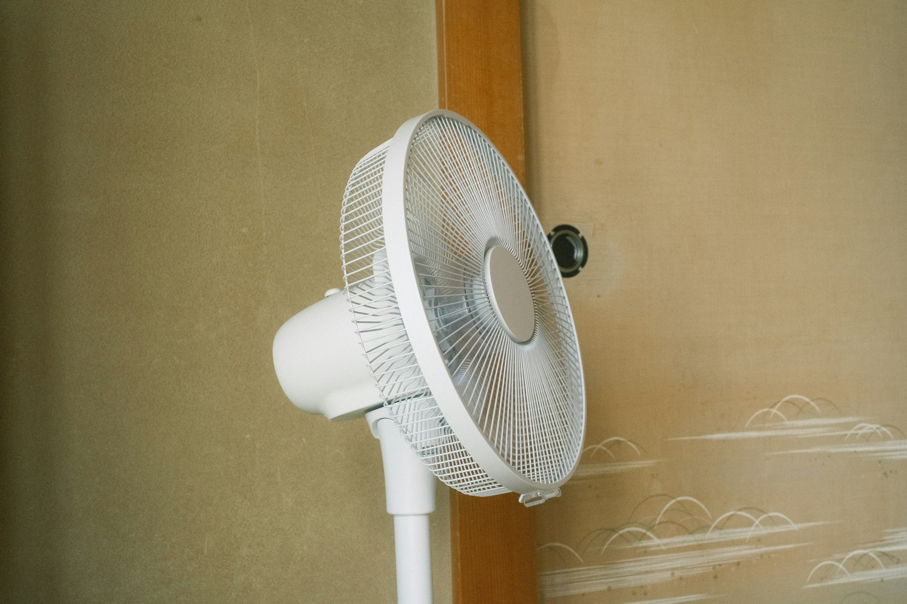 Ein weißer Ventilator, der in einer einfachen Innenumgebung nahe einer Wand positioniert ist