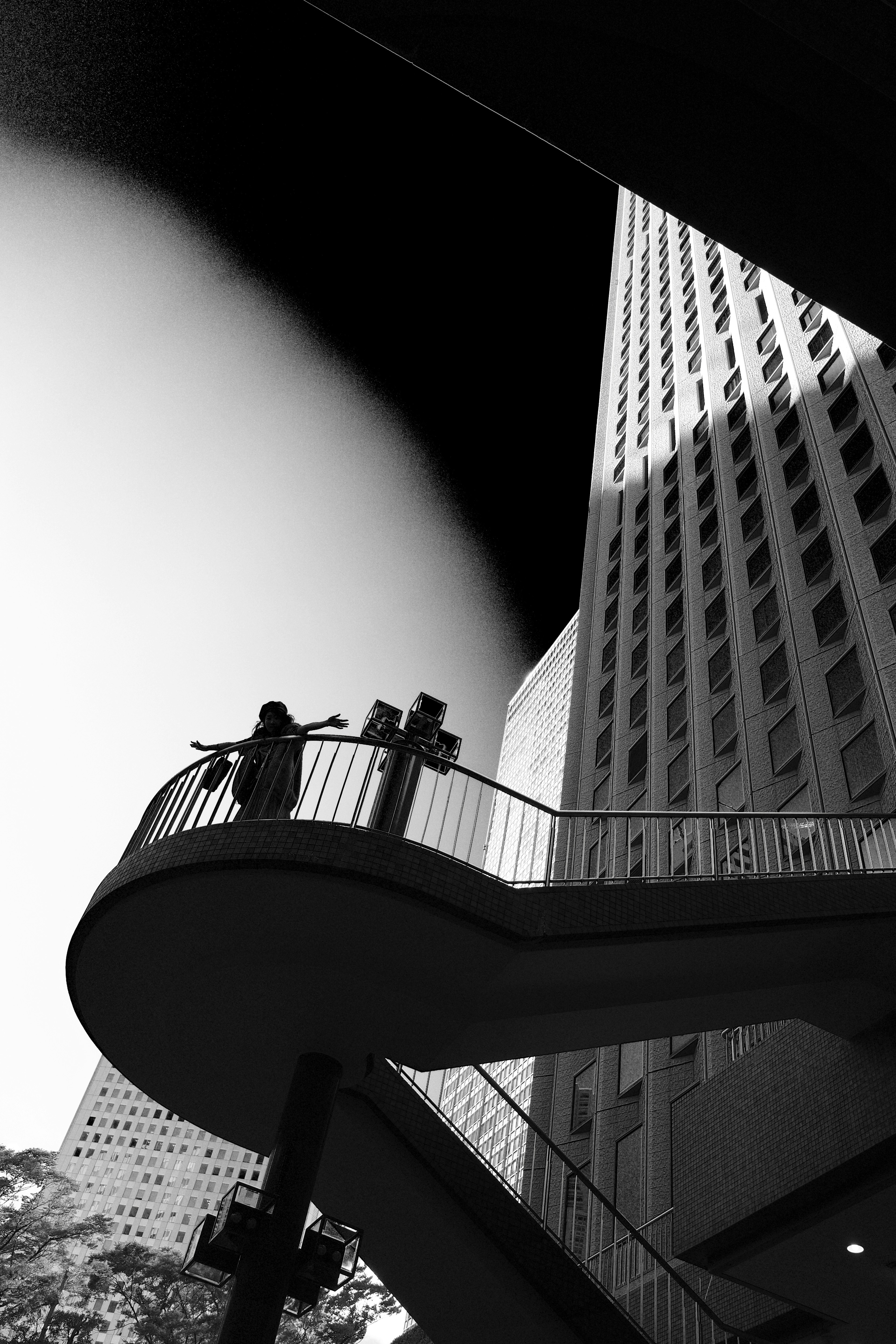 Schwarzweißfoto einer Treppe und eines Wolkenkratzers mit der Silhouette einer Person, die die Arme ausbreitet