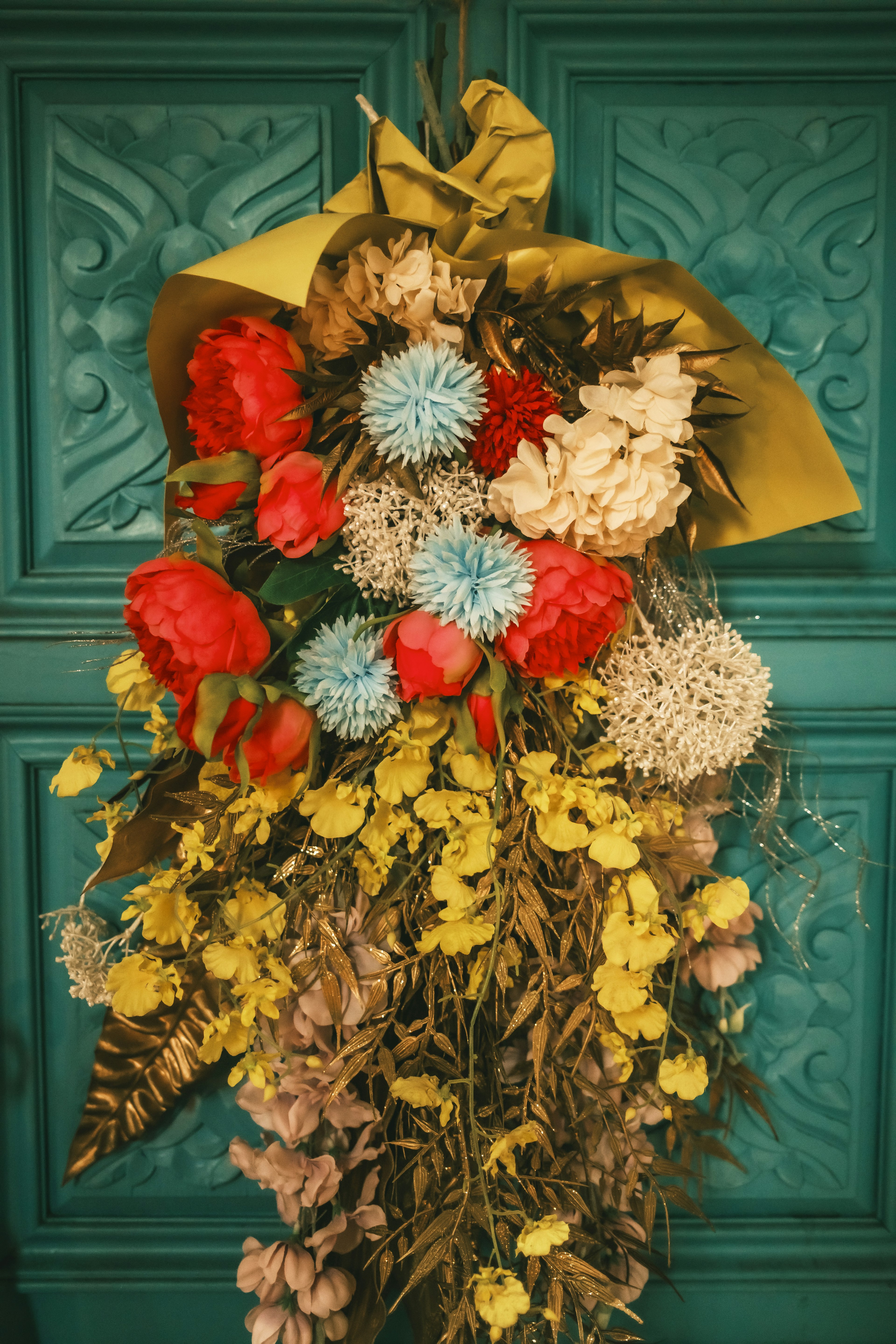 Colorful dried flower arrangement hanging on a teal door