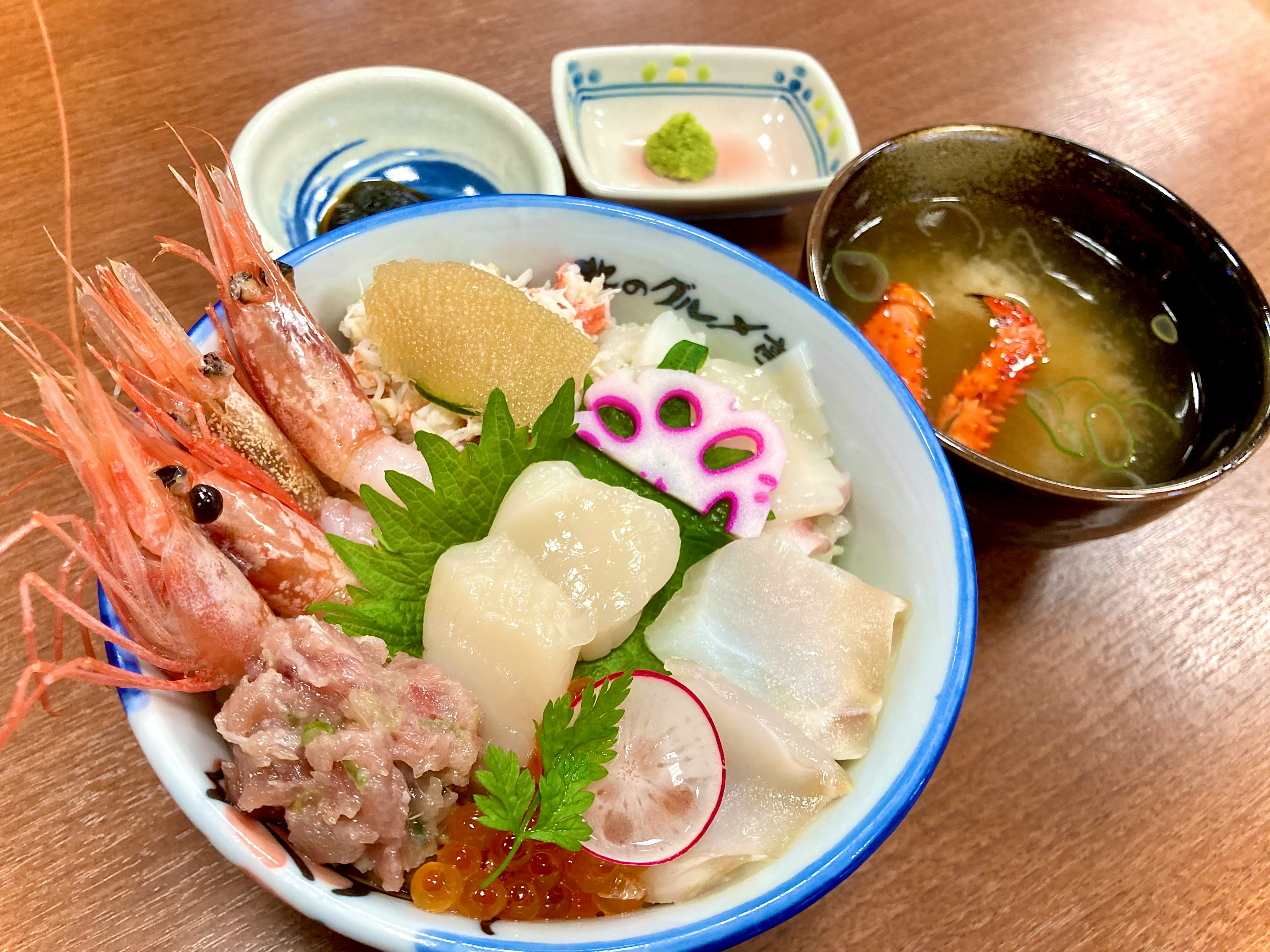 A colorful seafood bowl featuring shrimp, scallops, ikura, and garnished with wasabi