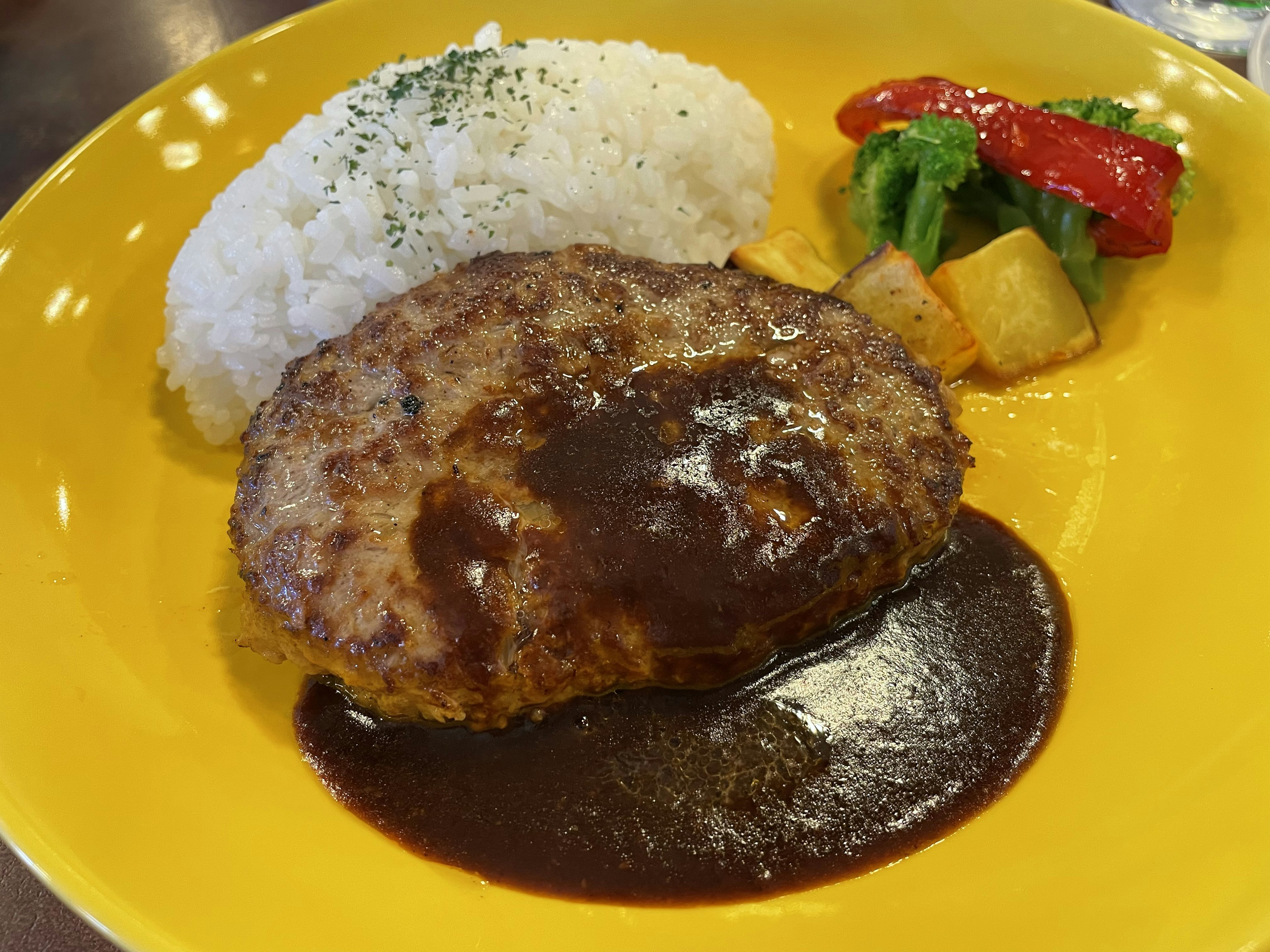 Un steak haché sur une assiette jaune avec du riz blanc et des légumes colorés