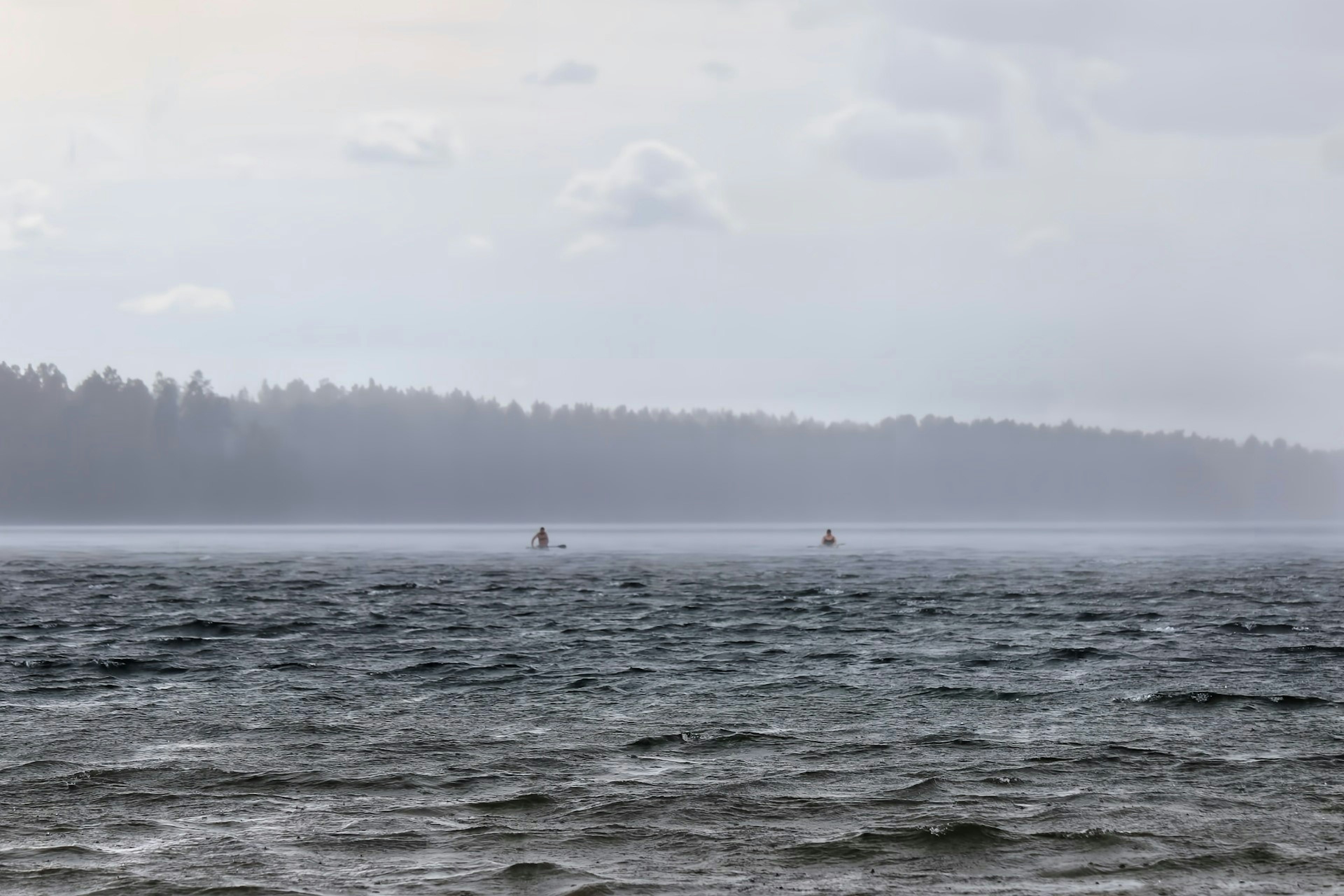 A misty lake scene with small boats in the distance